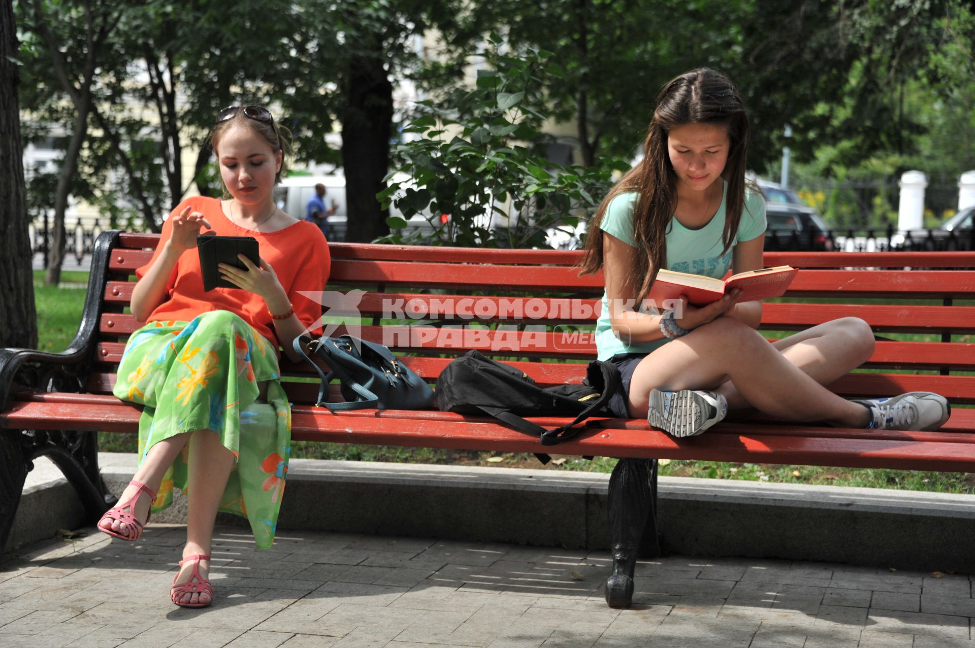 Москва.  Девушки читают книги, сидя на скамейке в парке.