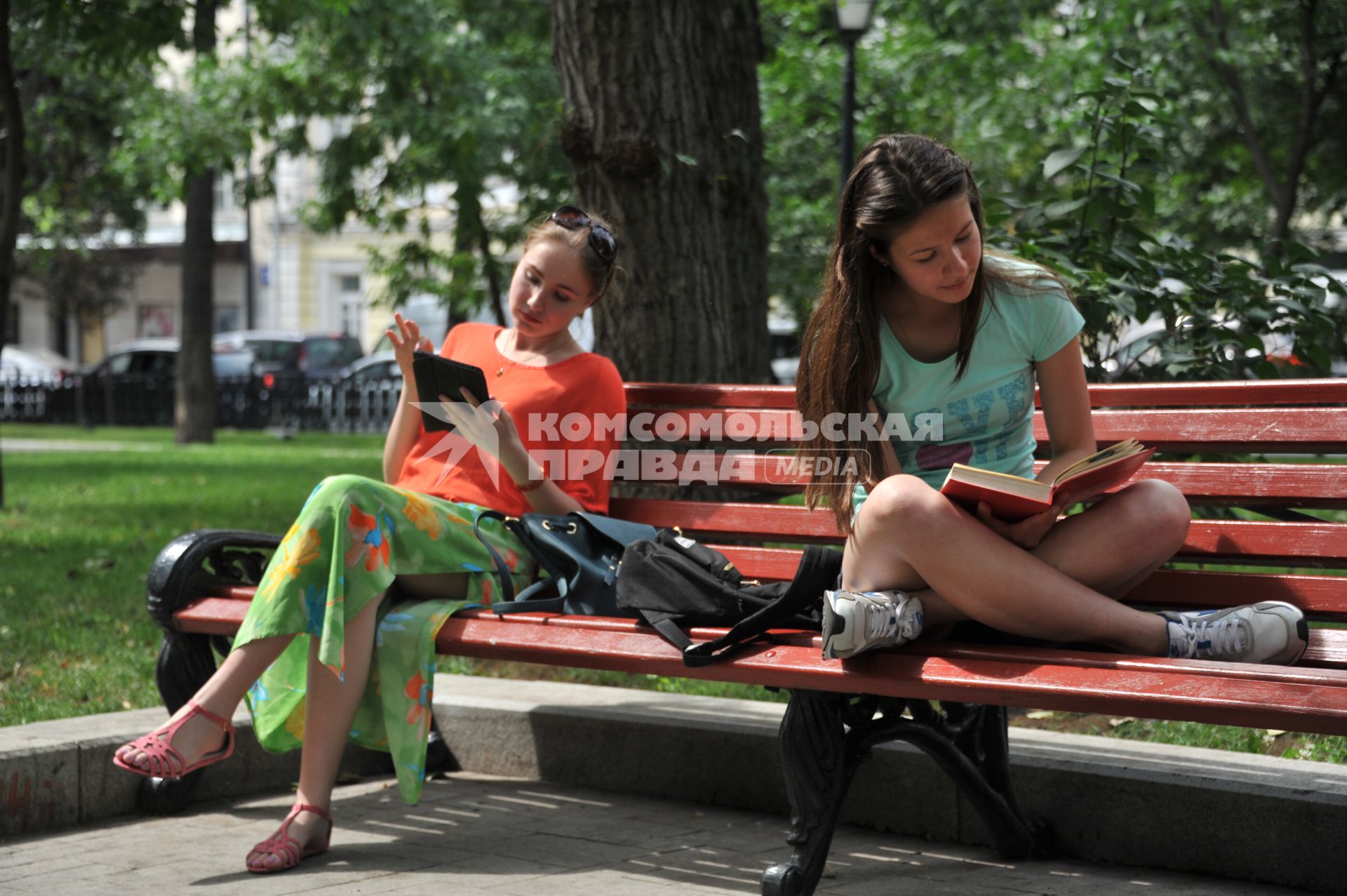 Москва.  Девушки читают книги, сидя на скамейке в парке.