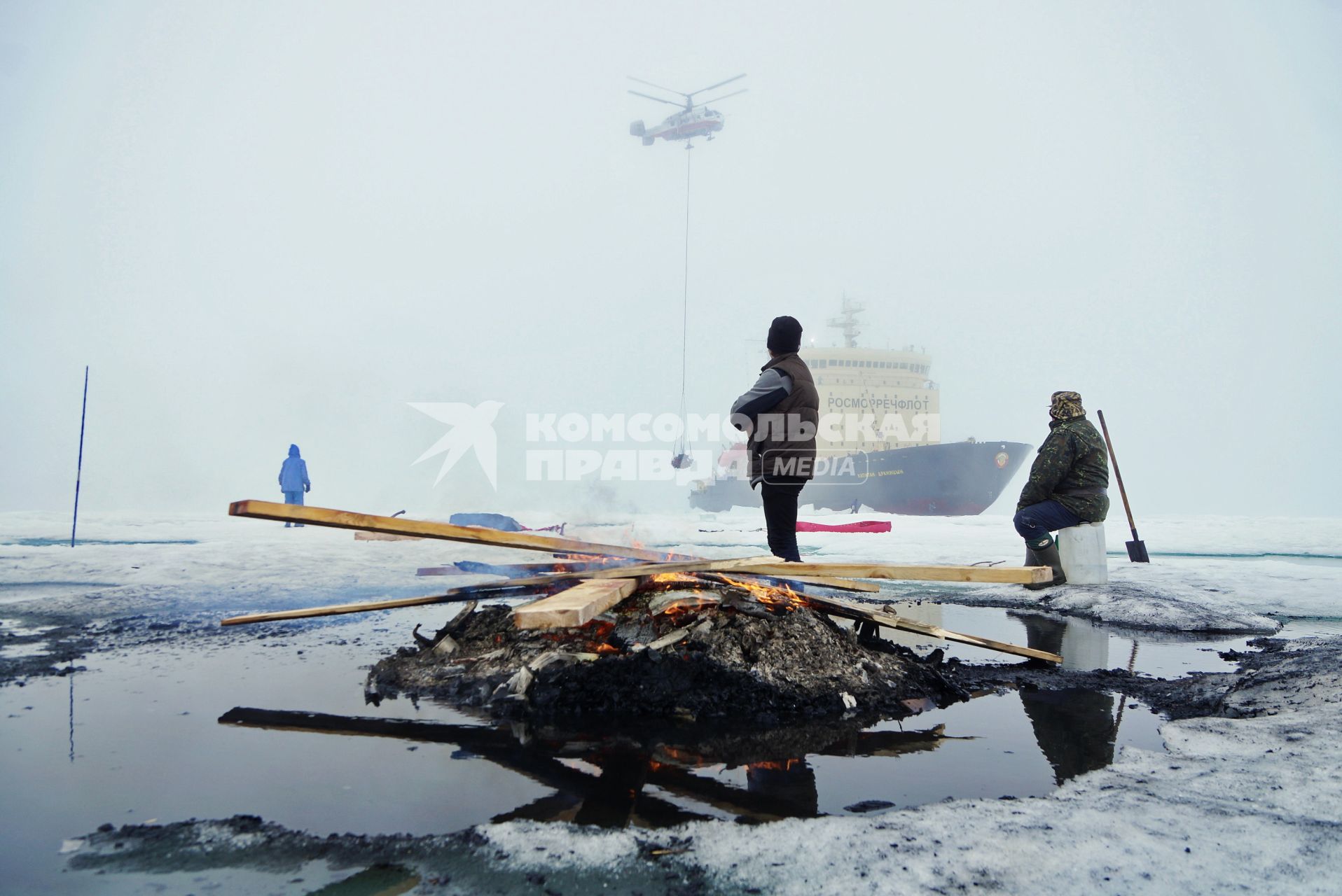 Полярники у костра из остатков стройматериалов и мусора, наблюдают как вертолет Ка-32 МЧС России перевозит аппаратуру и имущество с сезонной дрейфующей станции \"Северный полюс 2015\" из Арктики, на ледокол \"Капитан Драницын\" перед эвакуацией на большую землю. Северный полюс. Северный ледовитый океан