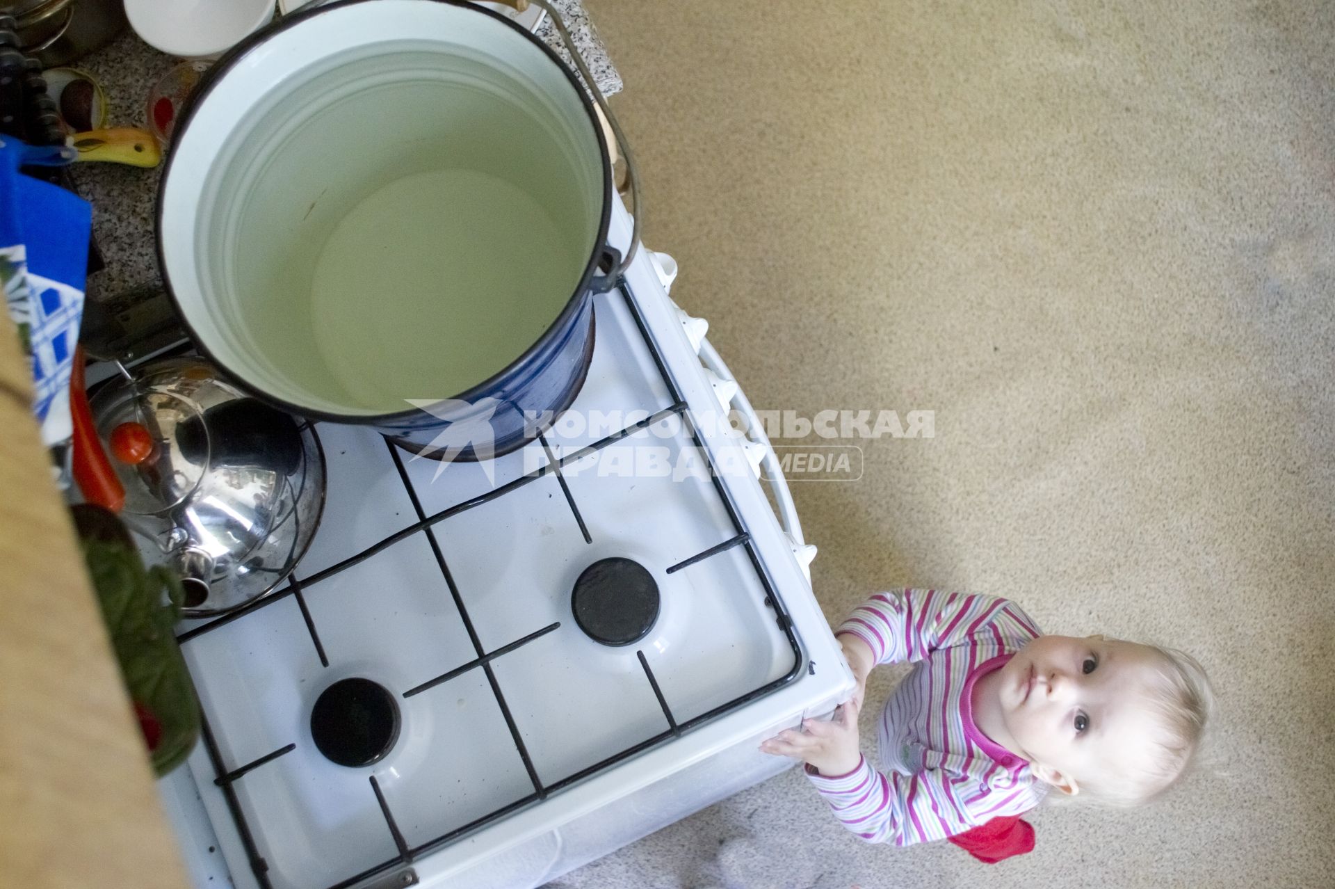 Маленький ребенок у газовой плиты, на которой греется вода в ведре для купания. Екатеринбург