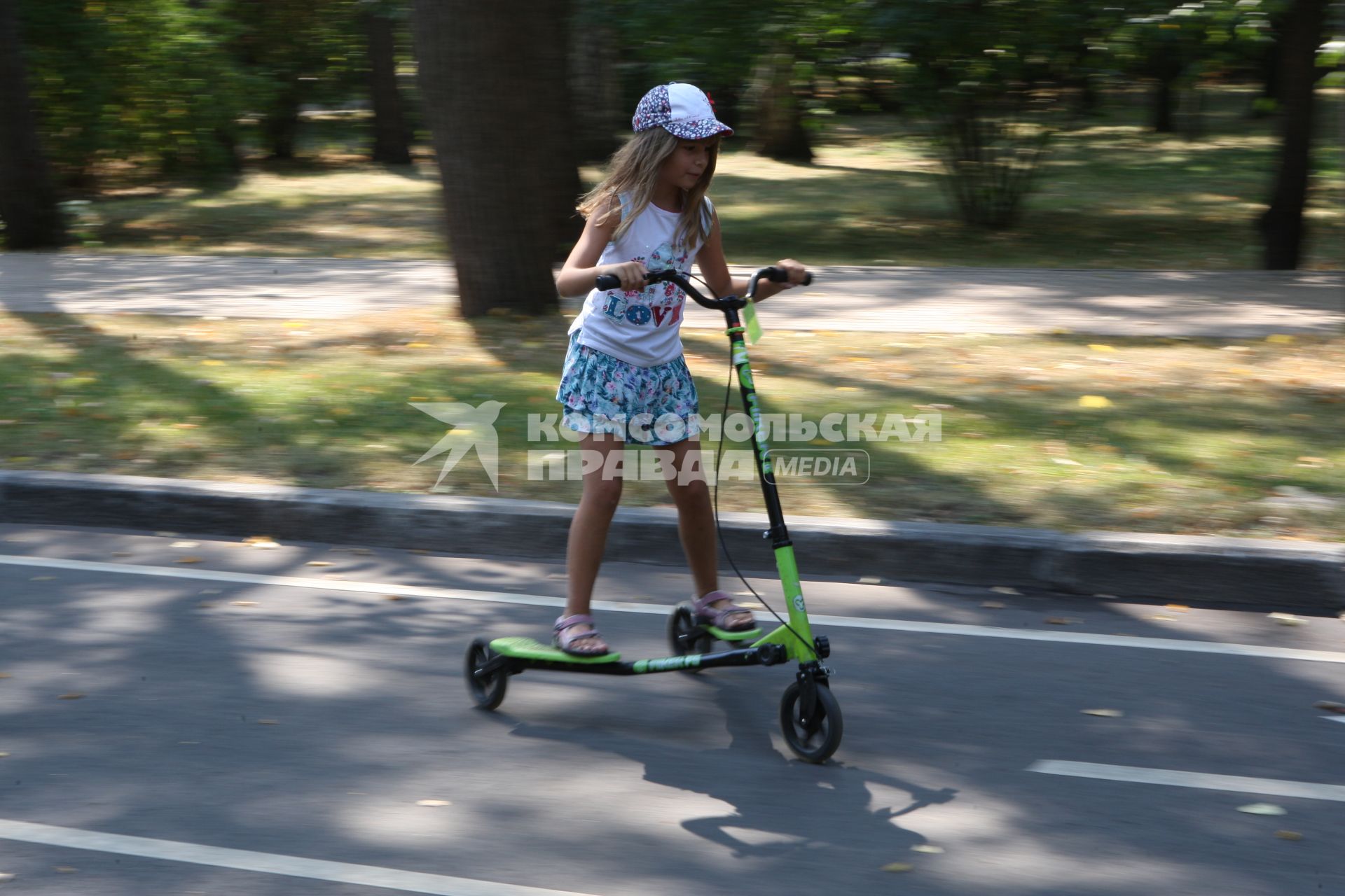 Москва. Девочка катается на техколесном самокате в парке `Сокольники`.