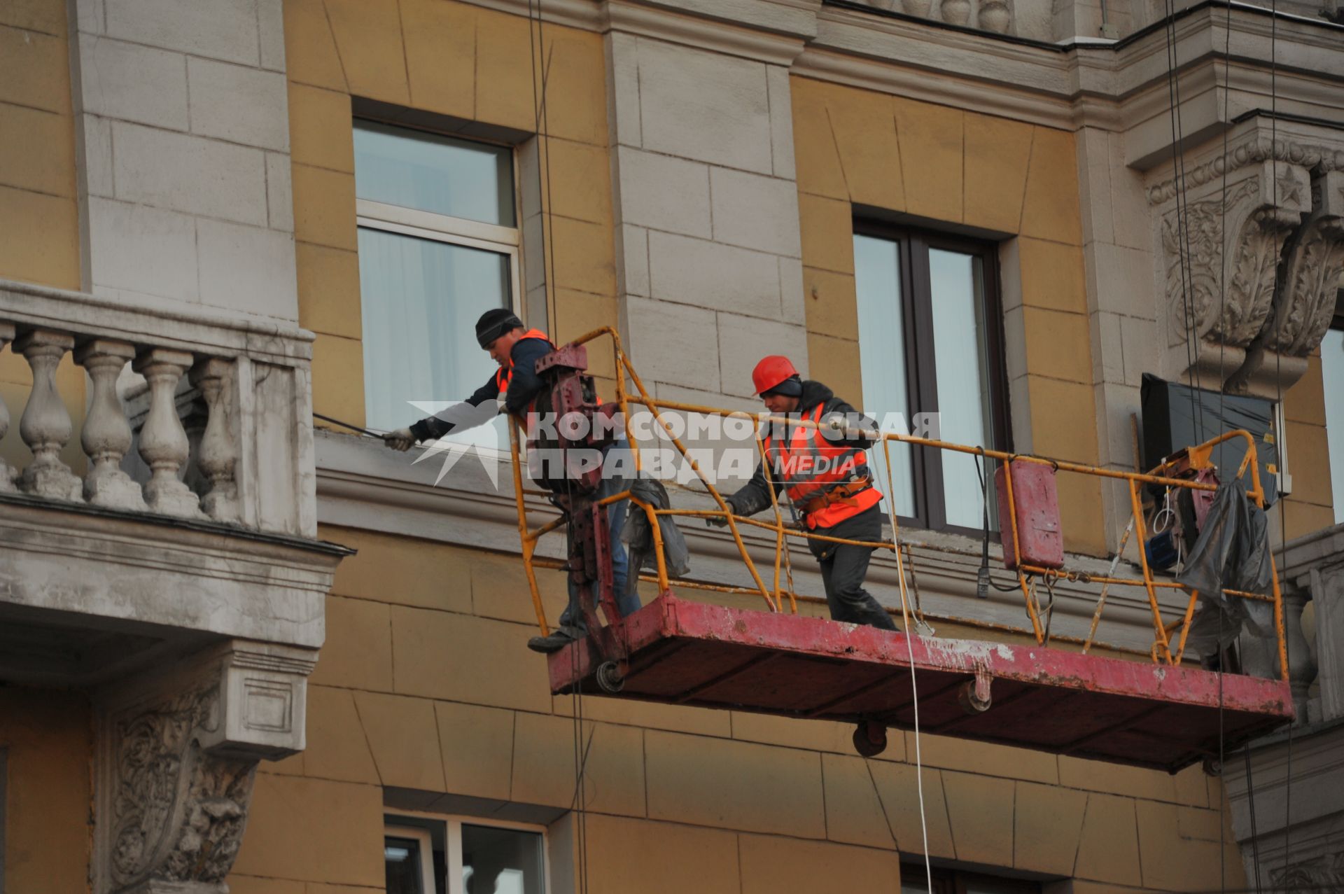 Москва.  Рабочие ремонтируют фасад здания.