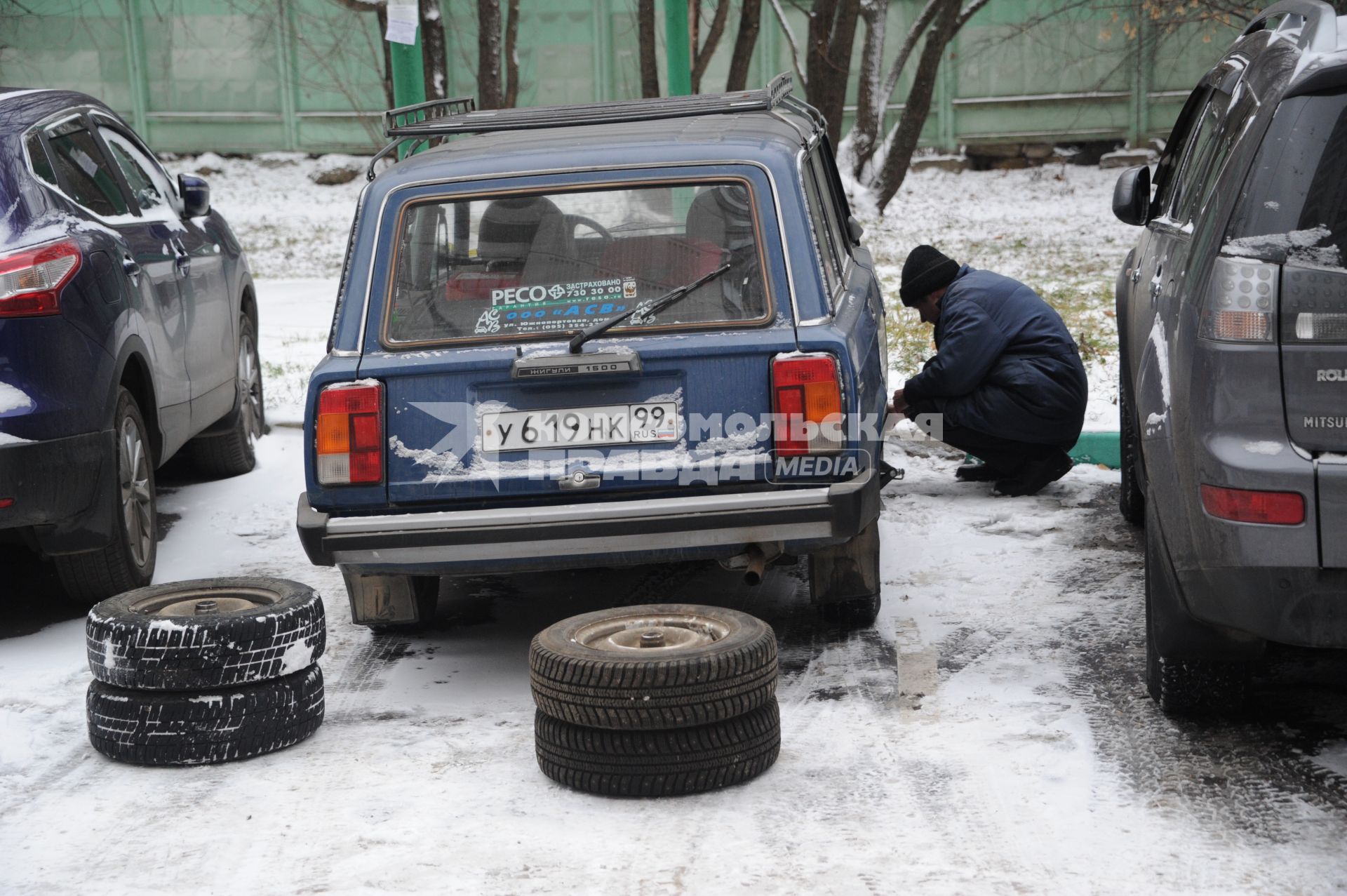 Москва.  Первый снег. Мужчина меняет колеса автомобиля.