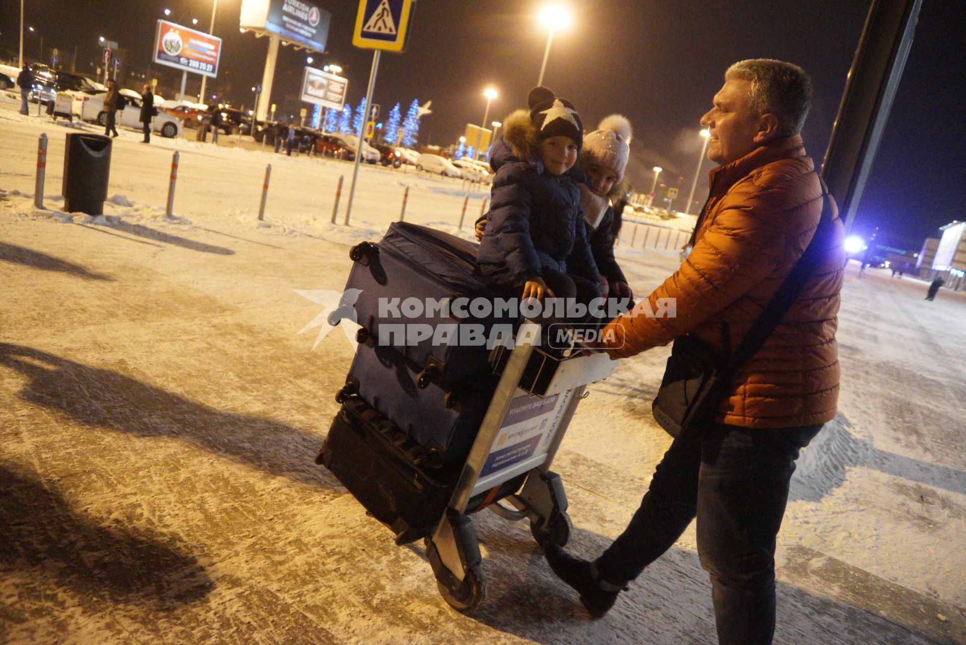 Екатеринбург. Аэропорт Кольцово. Мужчина везет детей, сидящих верхом на чемоданах.