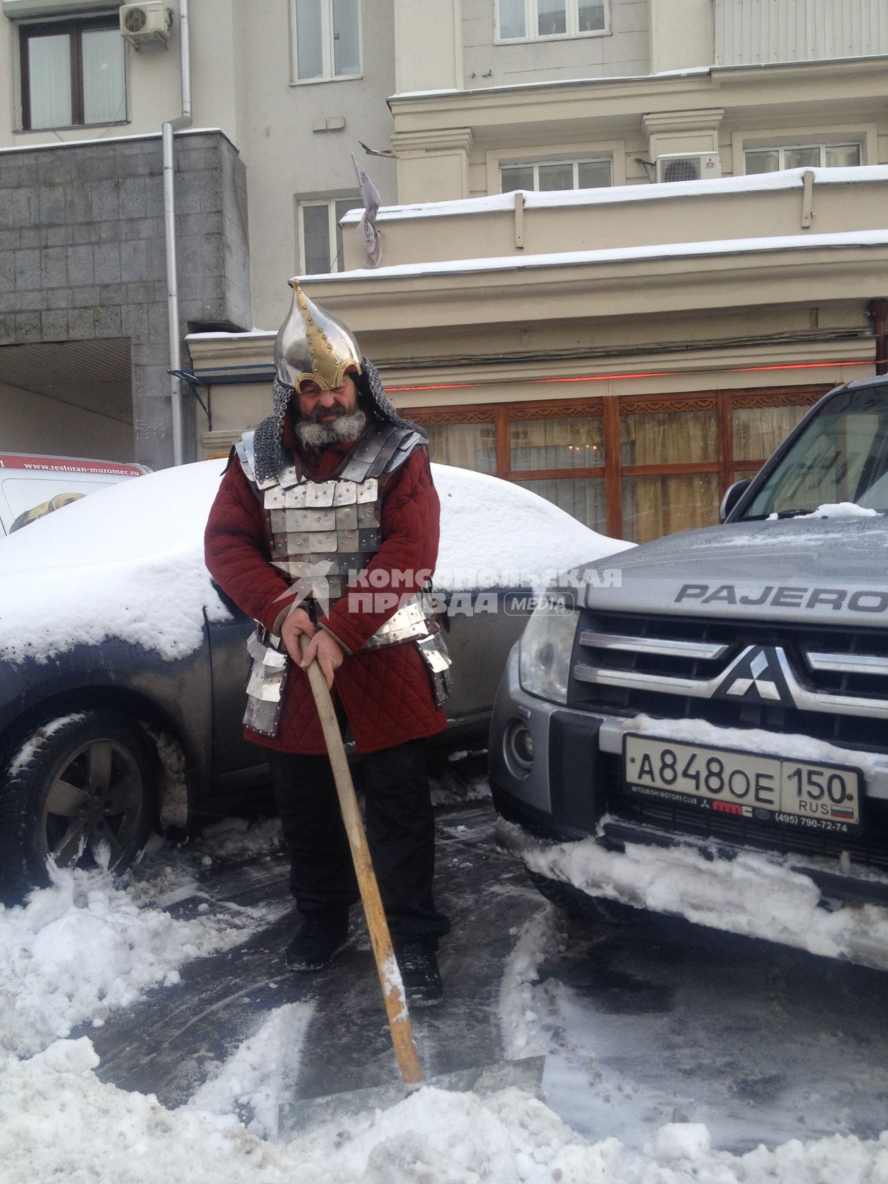 Москва. Мужчина в костюме русского былинного богатыря очищает снег около машины.