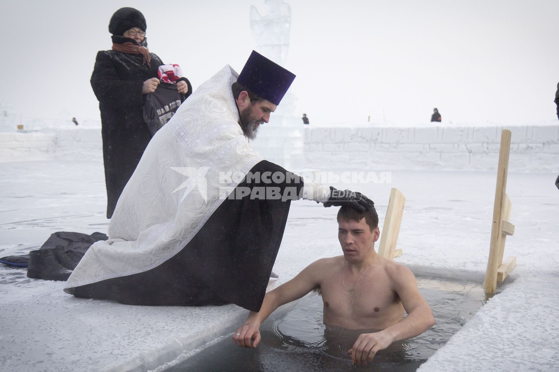 Крещенские купания в Иркутске. Священнослужитель окунает юношу в прорубь.