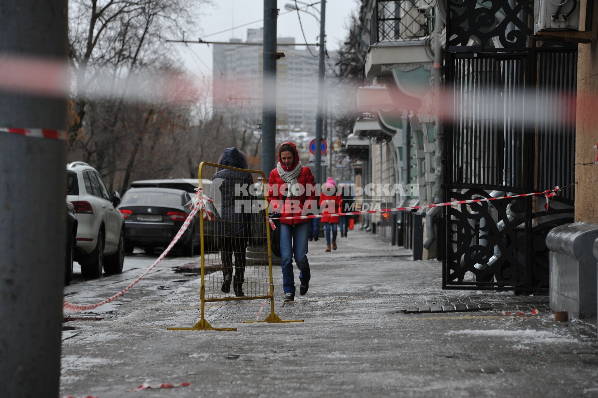 Москва.  Женщина идет по тротуару мимо оградительной ленты.