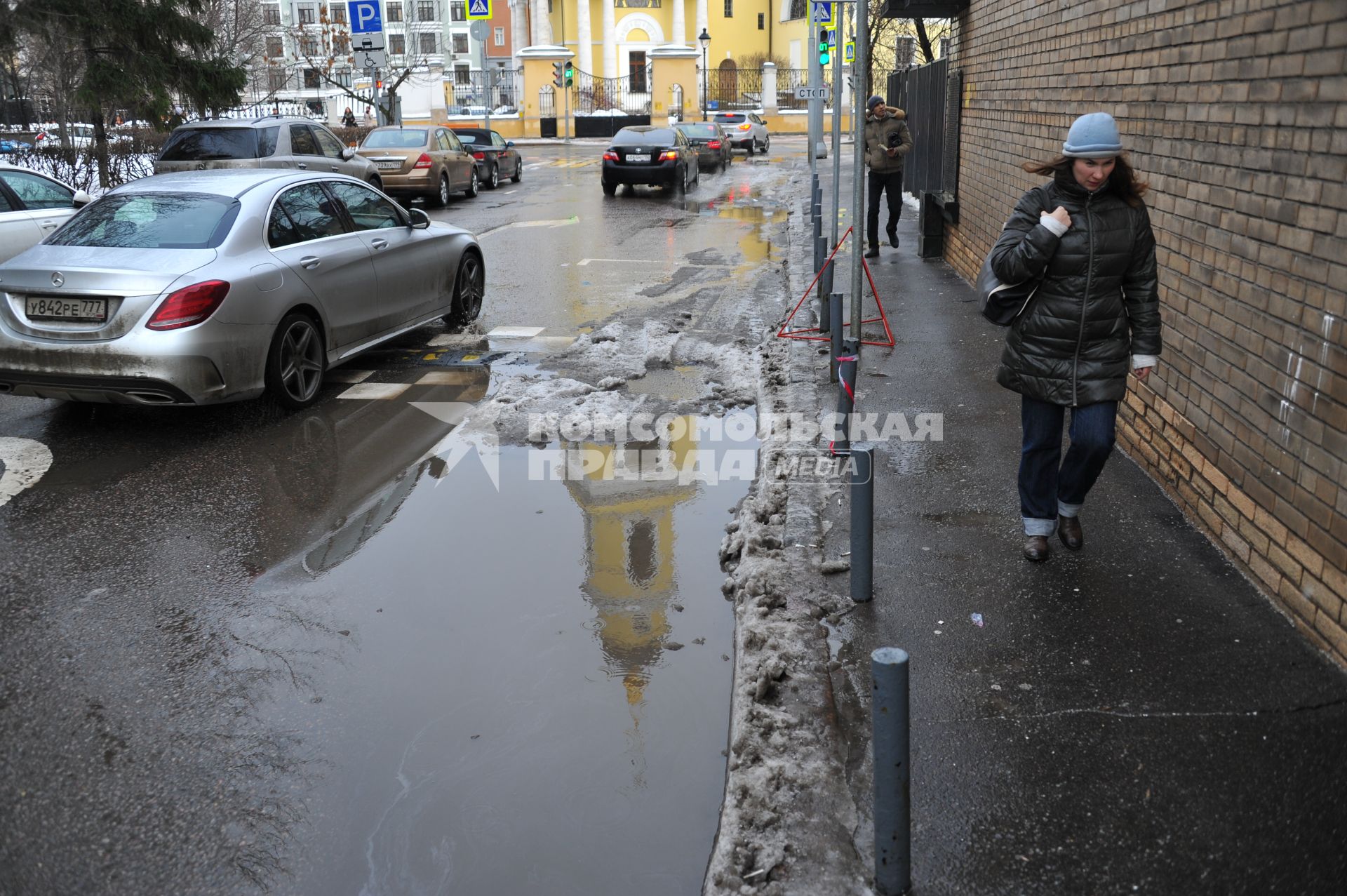 Москва.  Женщина идет по тротуару вдоль дороги.