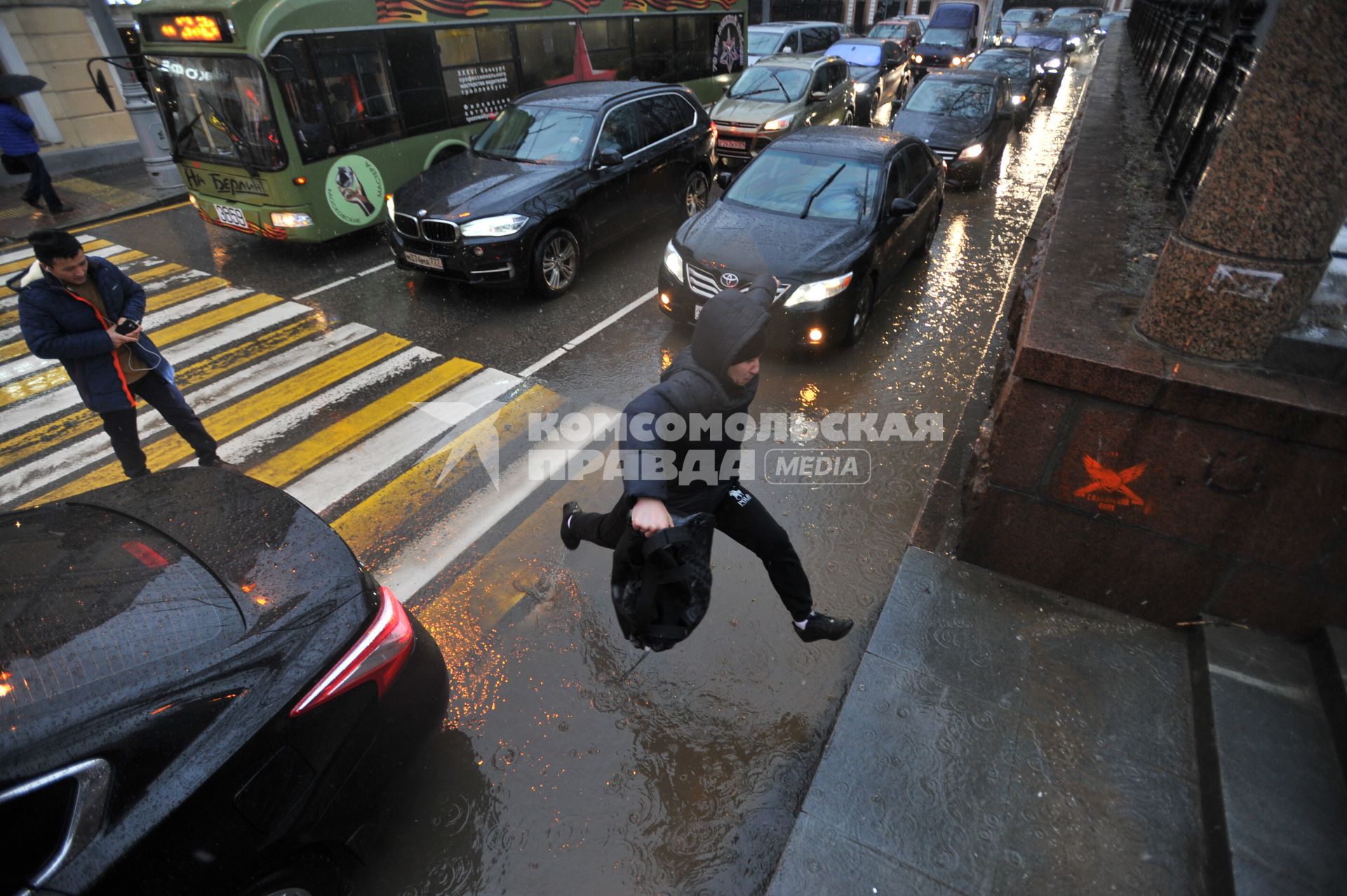 Москва.  Мужчина прыгает через лужу на пешеходном переходе  на Гоголевском бульваре.