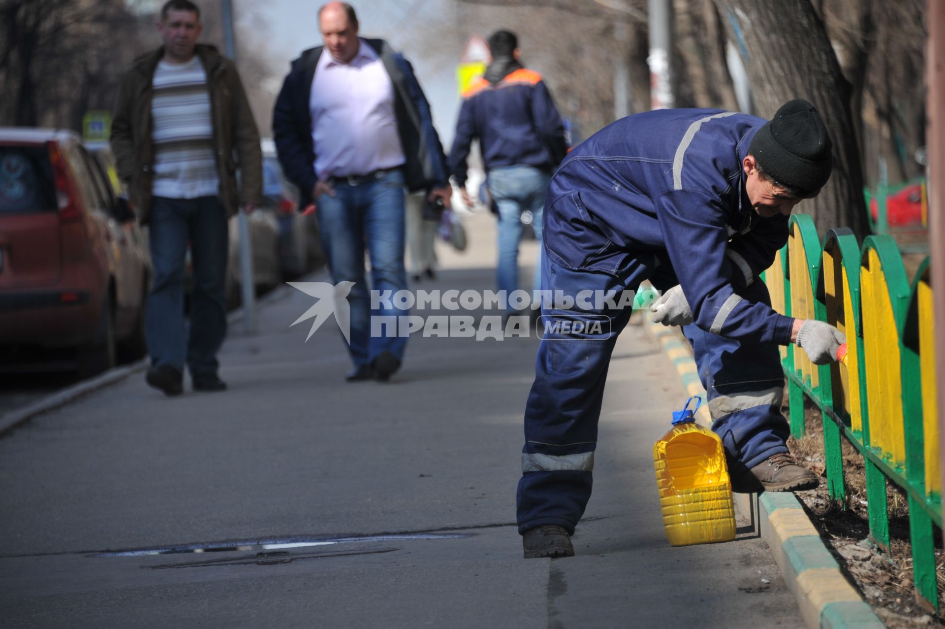 Москва.  Сотрудник коммунальной службы красит  забор.