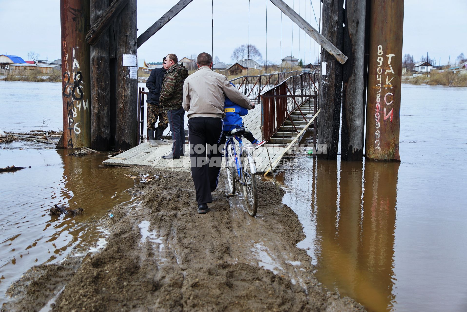Свердловская область, деревня Махнево. Мужчина с ребенком на велосипеде у подвесного моста во время разлива реки Тагил.