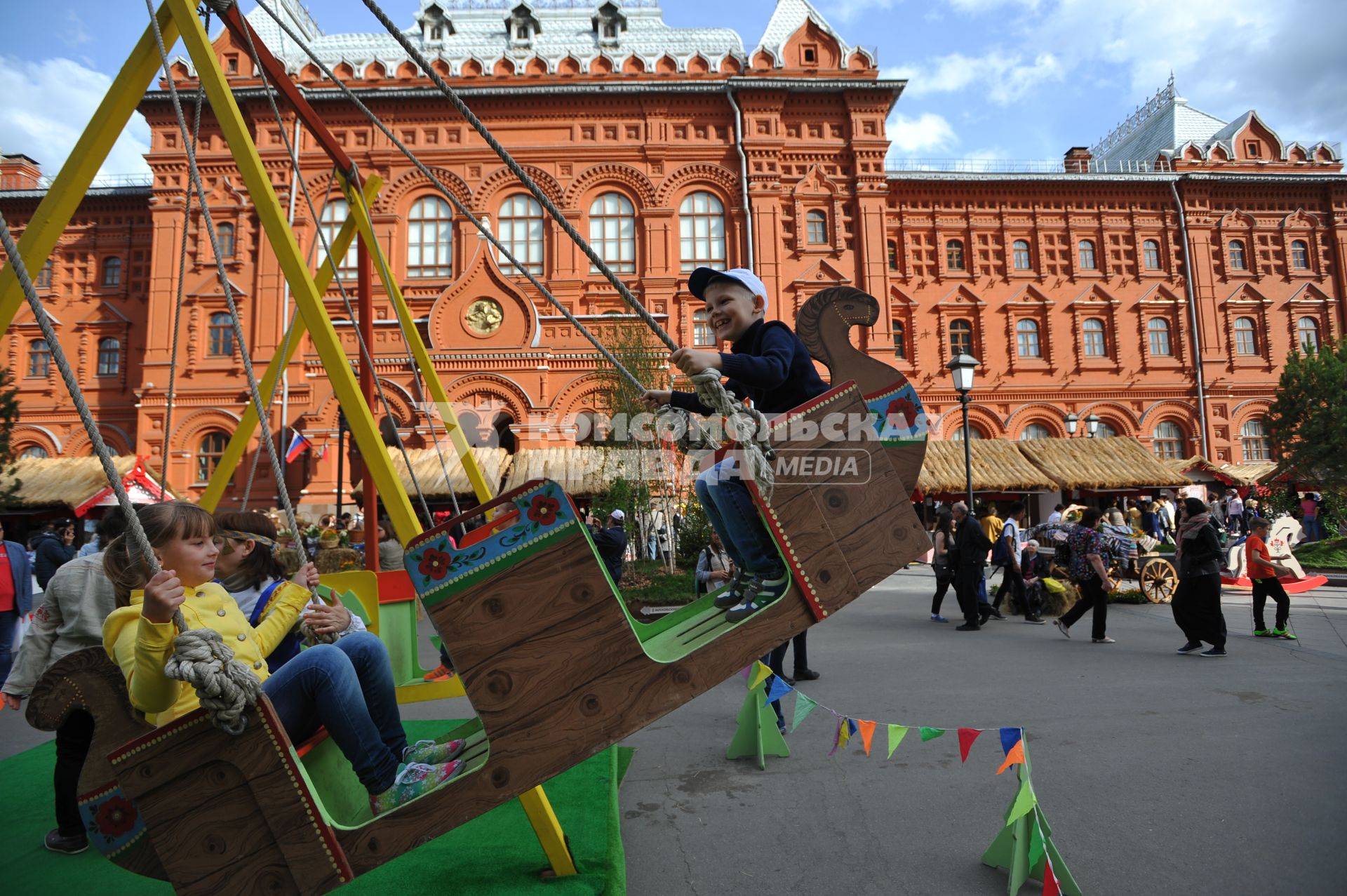 Москва.   Дети качаются на   деревянных качелях  на  историко-гастрономическом  фестивале `Наш продукт` в рамках уличных праздников `Московские сезоны` на Площади Революции.