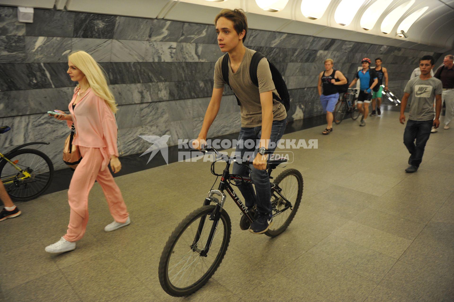Москва.  Молодой человек едет на велосипеде по платформе станции метро.