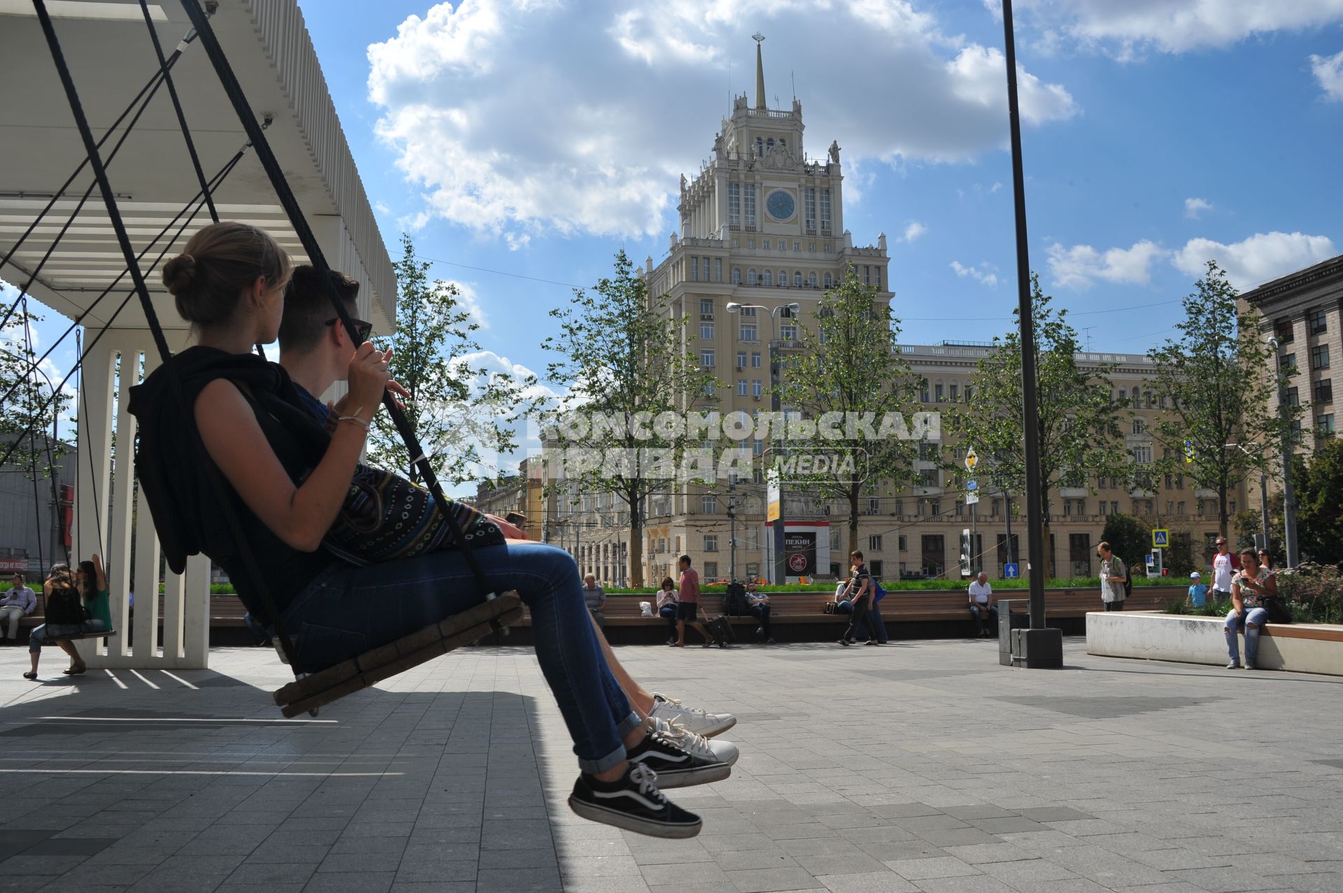 Москва.  Молодые люди  качаются на качелях на Триумфальной площади.