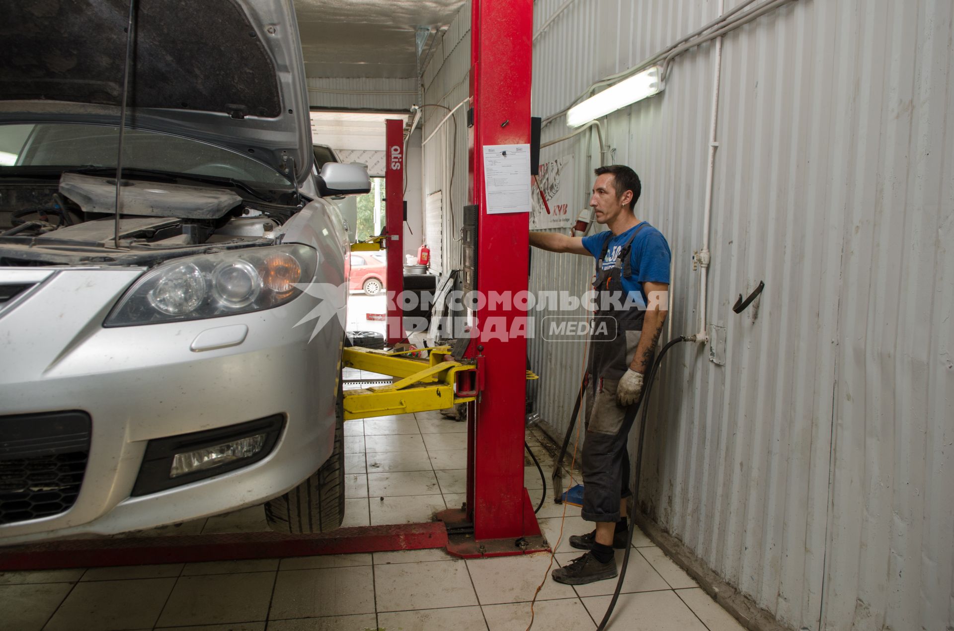 Самара.  Сотрудник автосервиса поднимает автомобиль на подъемнике.