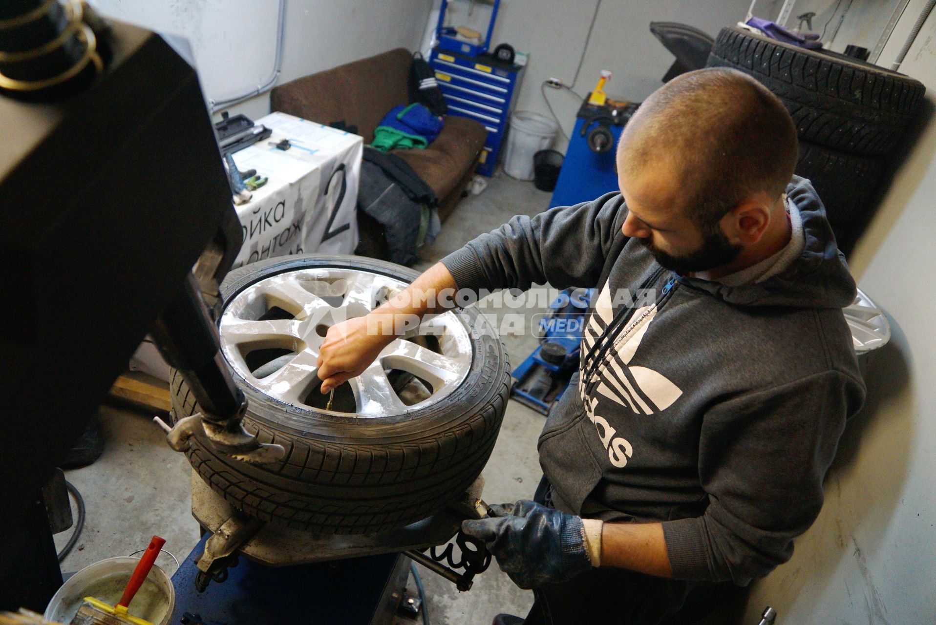 Екатеринбург. Сотрудник шиномонтажной мастерской бортует автомобильное колесо.
