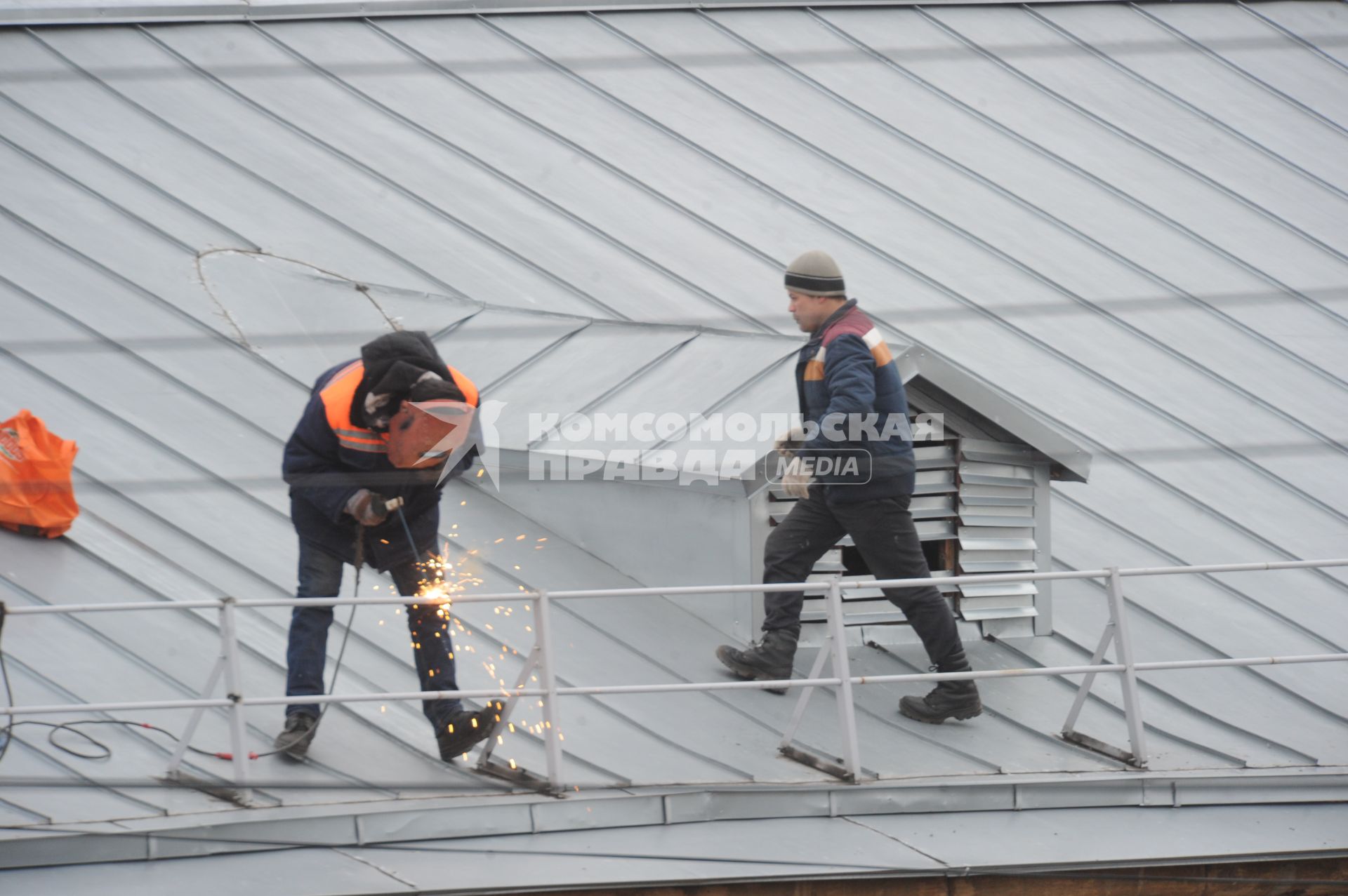 Москва.   Рабочий сваривает ограждение на крыше дома.