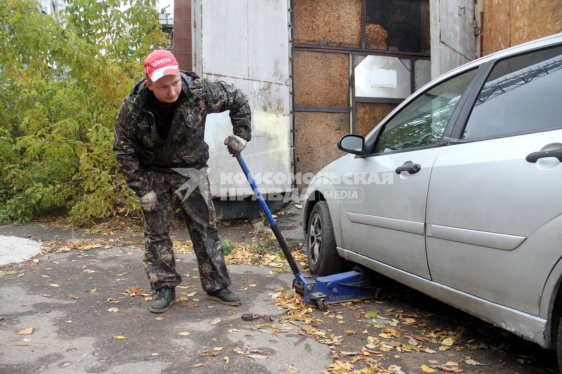 Нижний Новгород.  Работник шиномонтажной мастерской поднимает домкратом машину для замены колес.