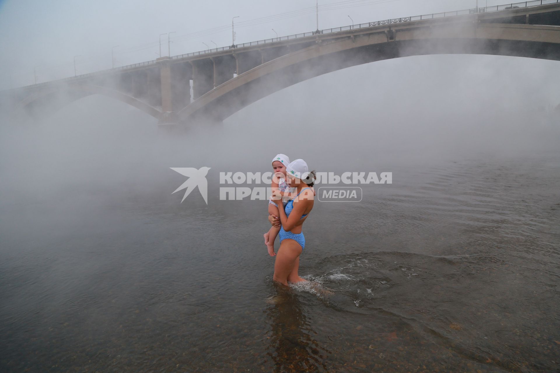 Красноярск. Женщина с ребенком окунается в реку.