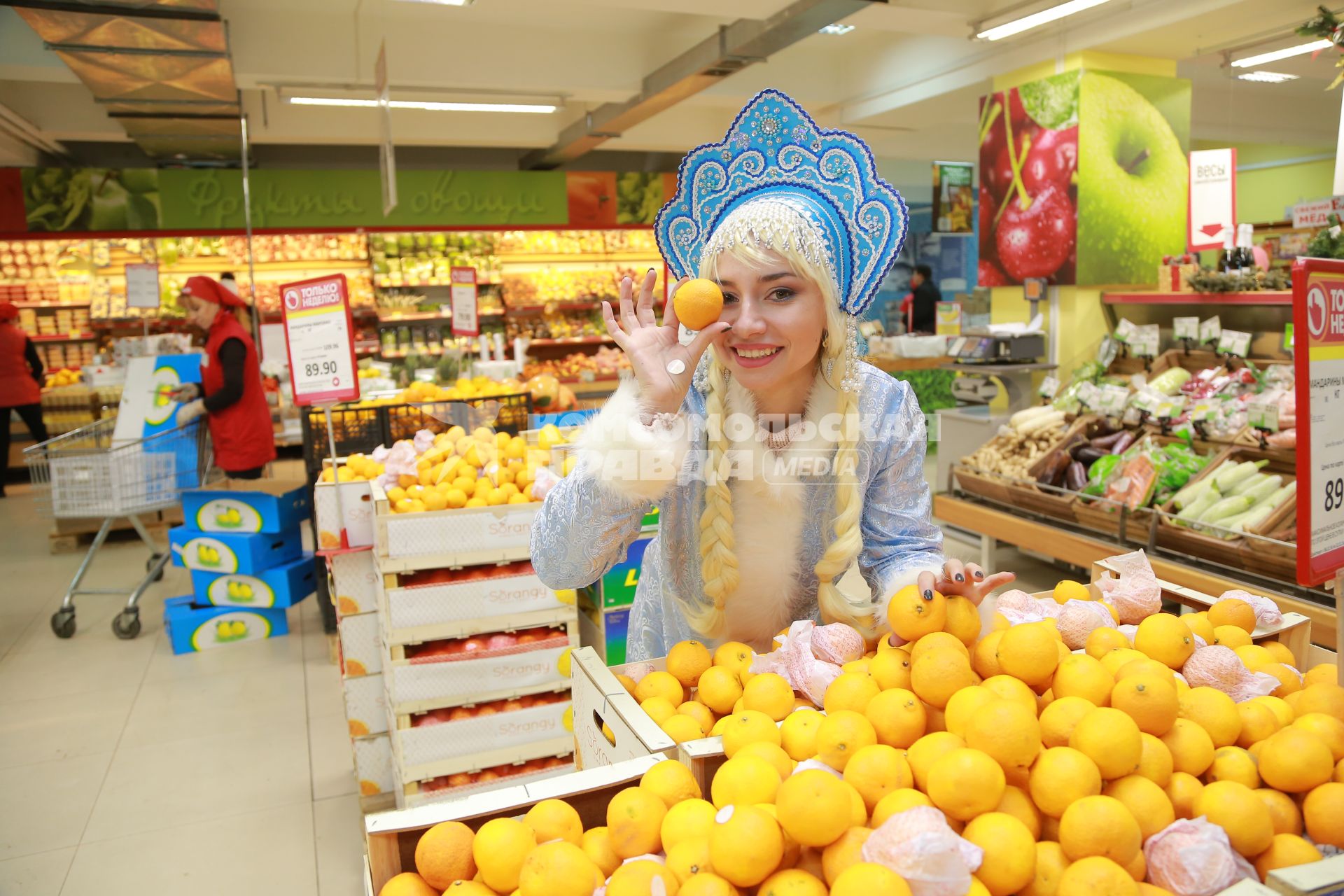 Красноярск. Девушка в костюме Снегурочки выбирает  мандарины в супермаркете.