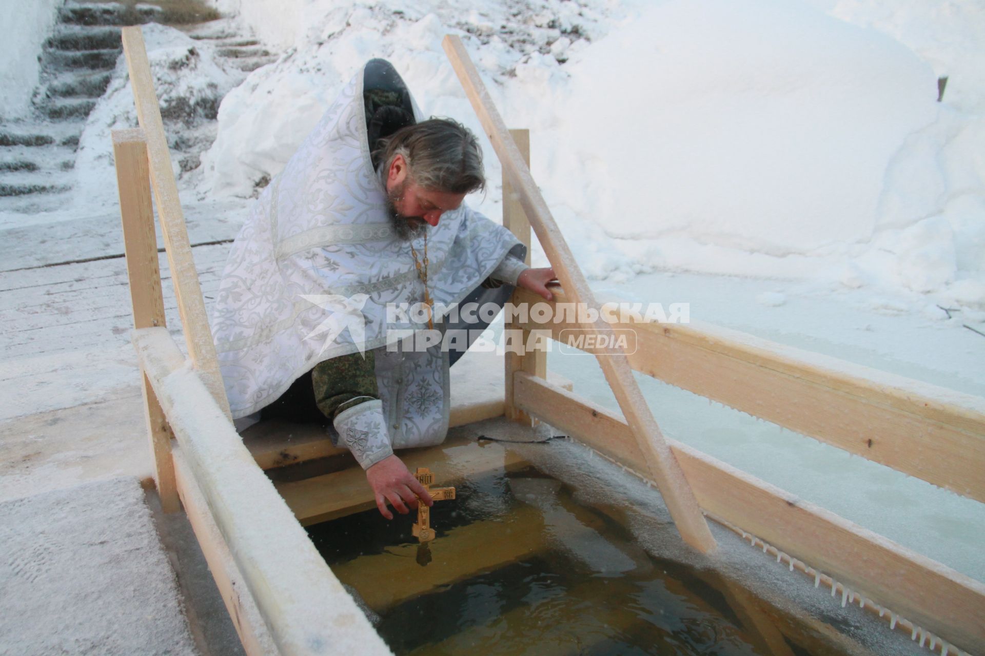 Алтайский край. Священнослужитель освящает воду в  проруби перед началом крещенского купания.