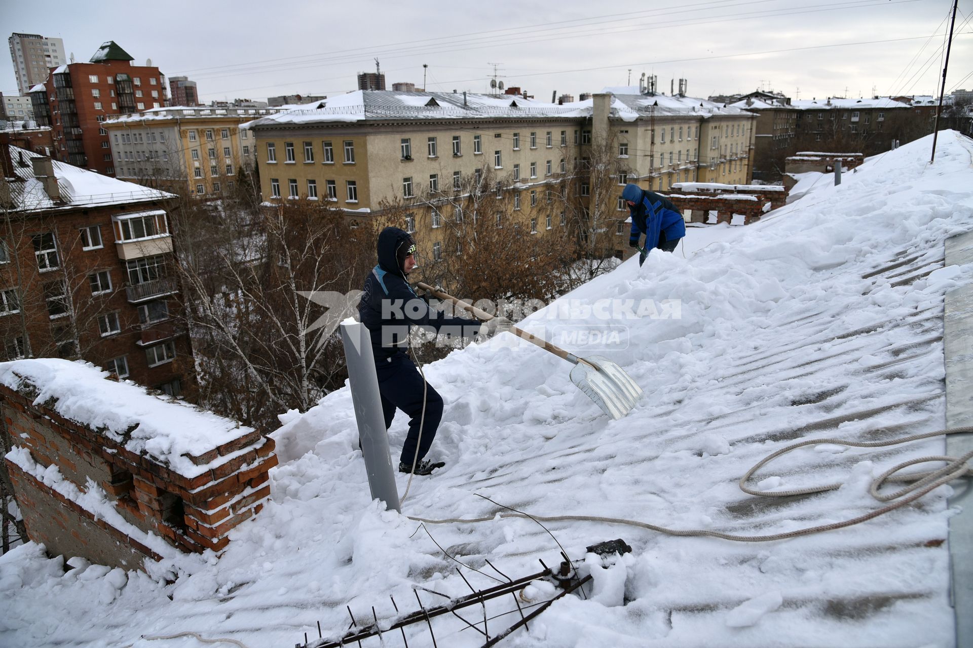 Новосибирск. Дворник на крыше лопатой счищает снег.