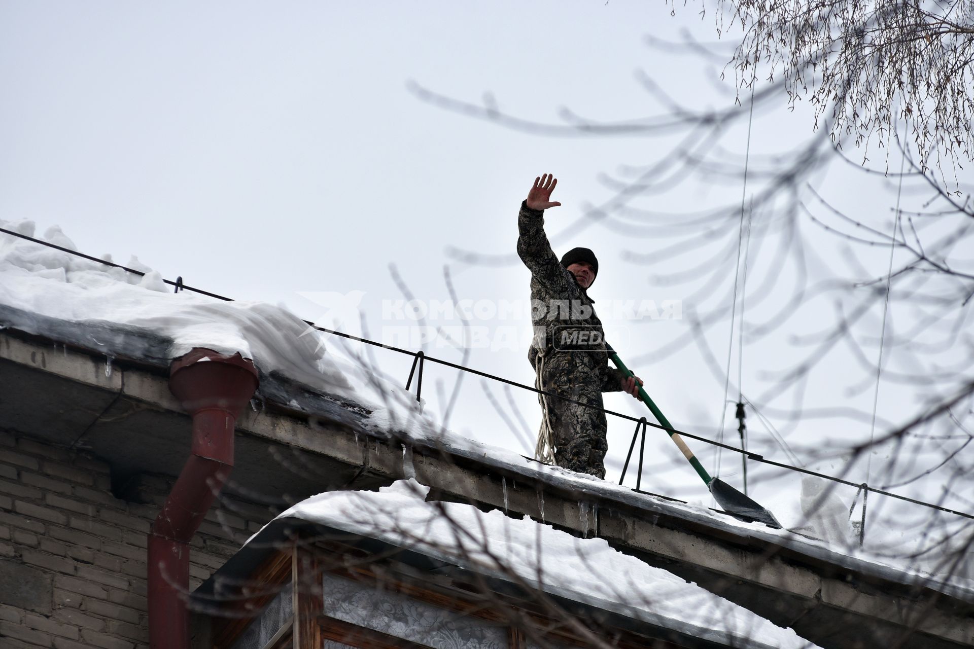 Новосибирск. Дворник  на крыше лопатой счищает снег.