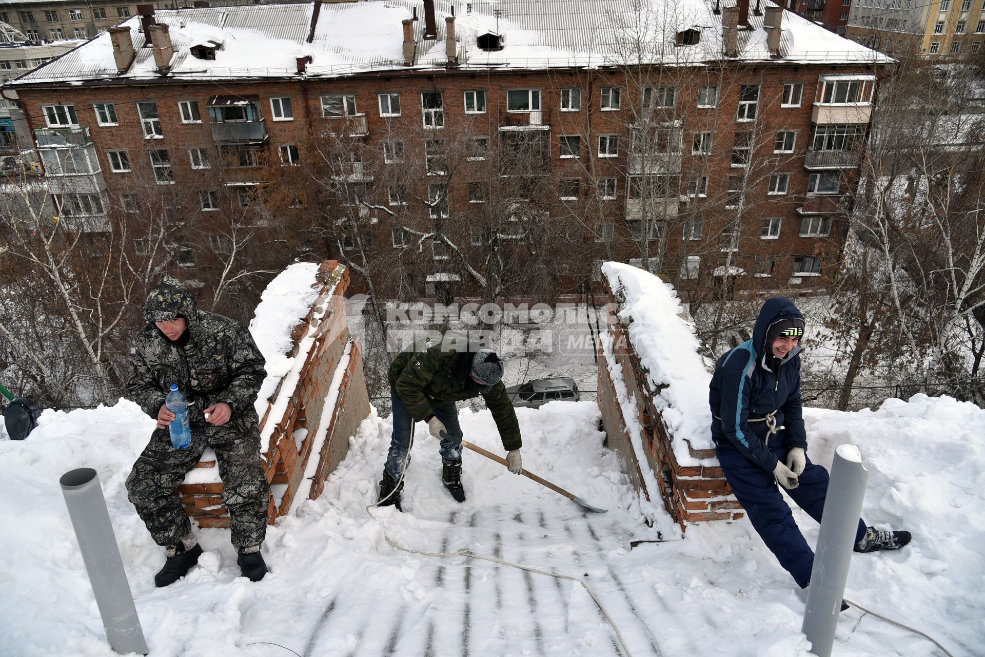 Новосибирск. Дворник на крыше лопатой счищает снег.