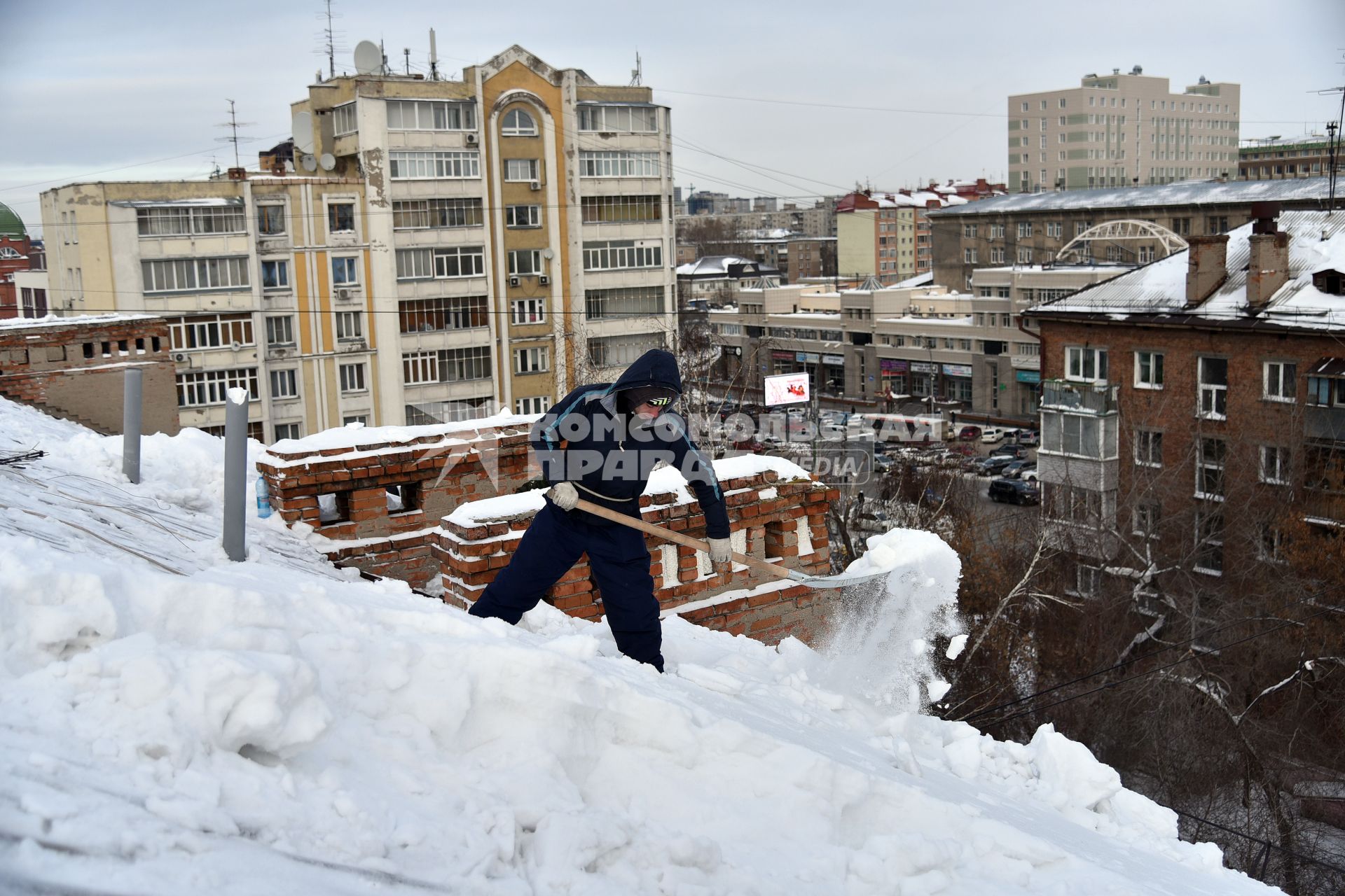 Новосибирск. Дворник  на крыше лопатой счищает снег.