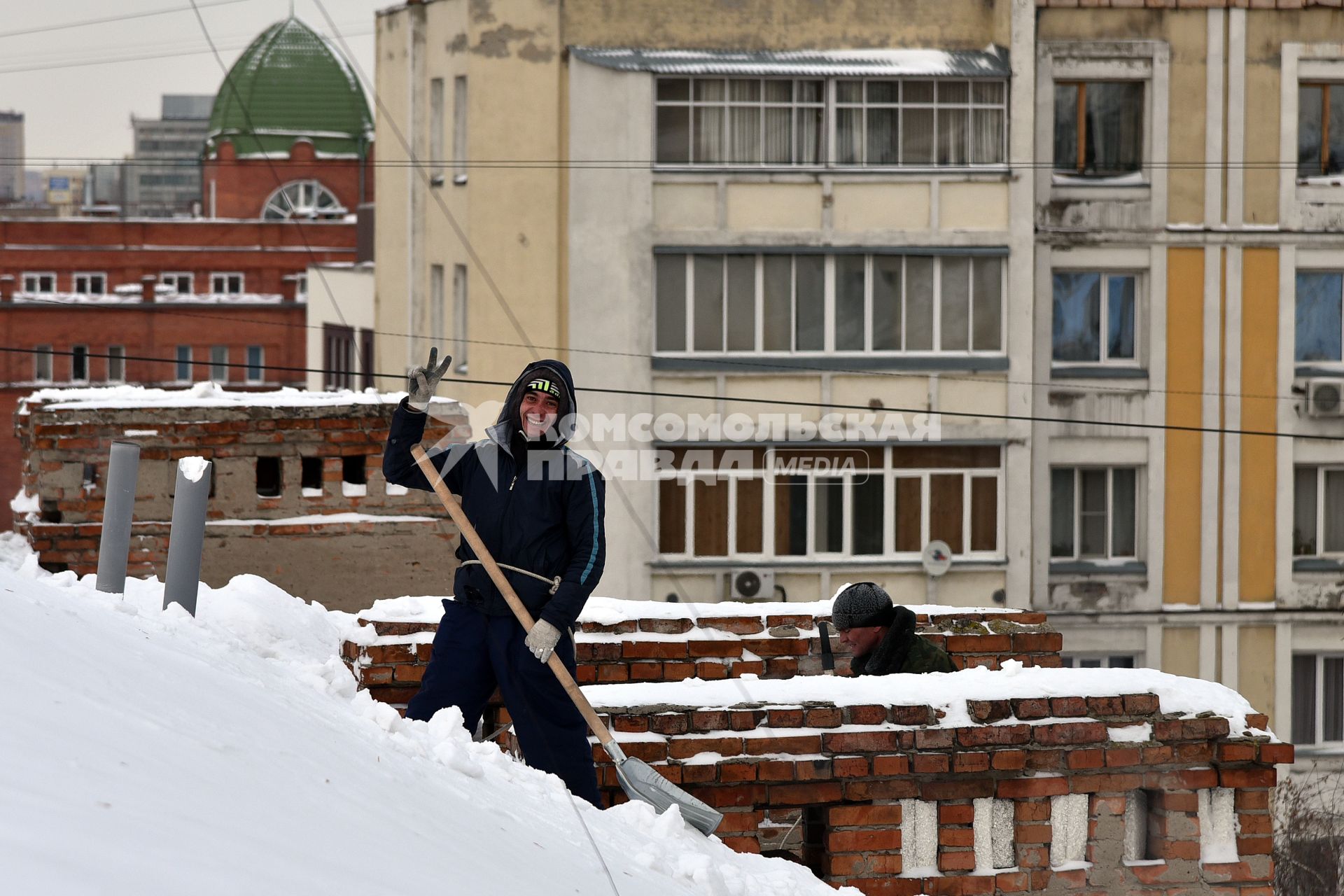 Новосибирск. Дворник на крыше лопатой счищает снег.