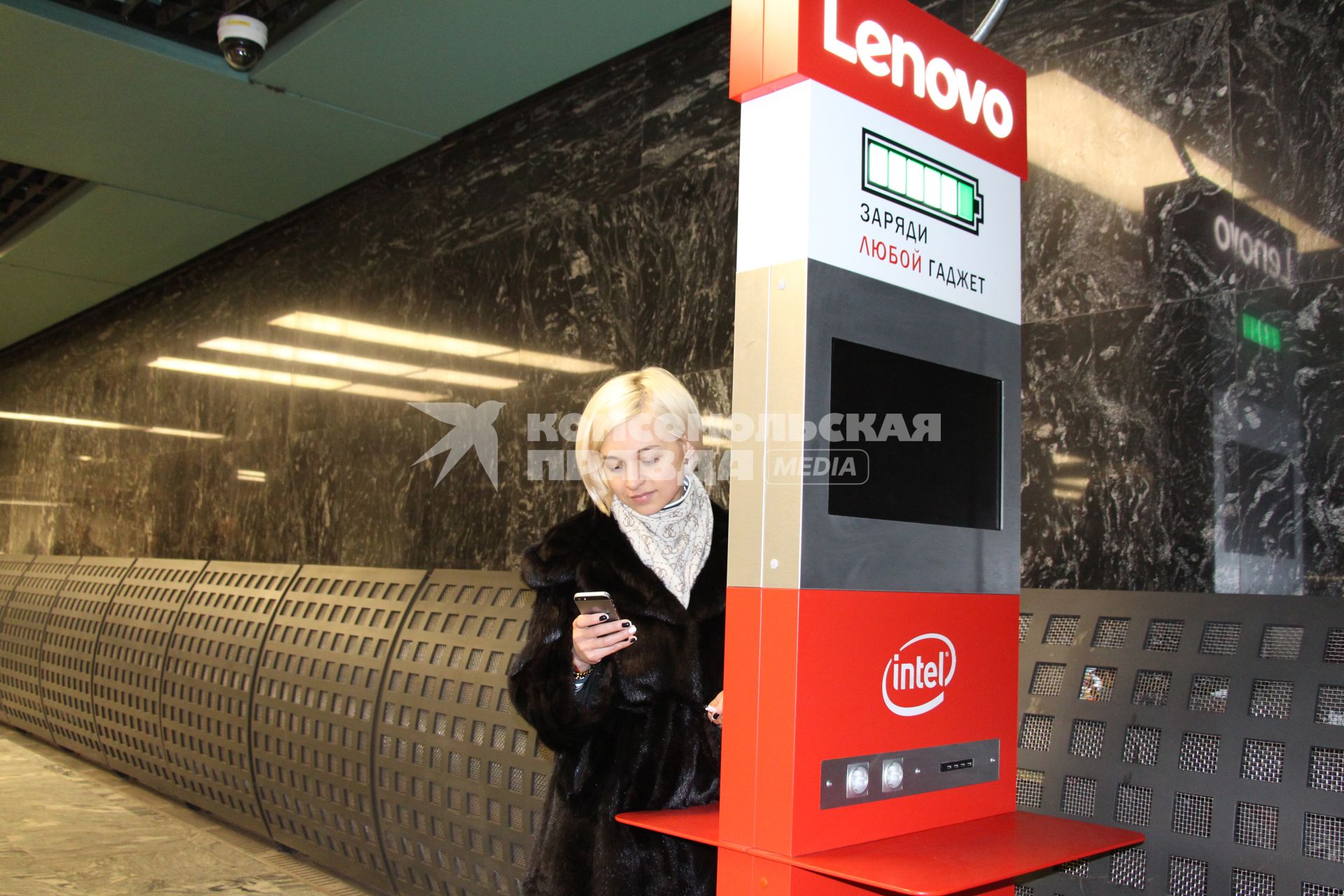 Москва. Девушка у стойки  для зарядки гаджета в вестибюле метро.
