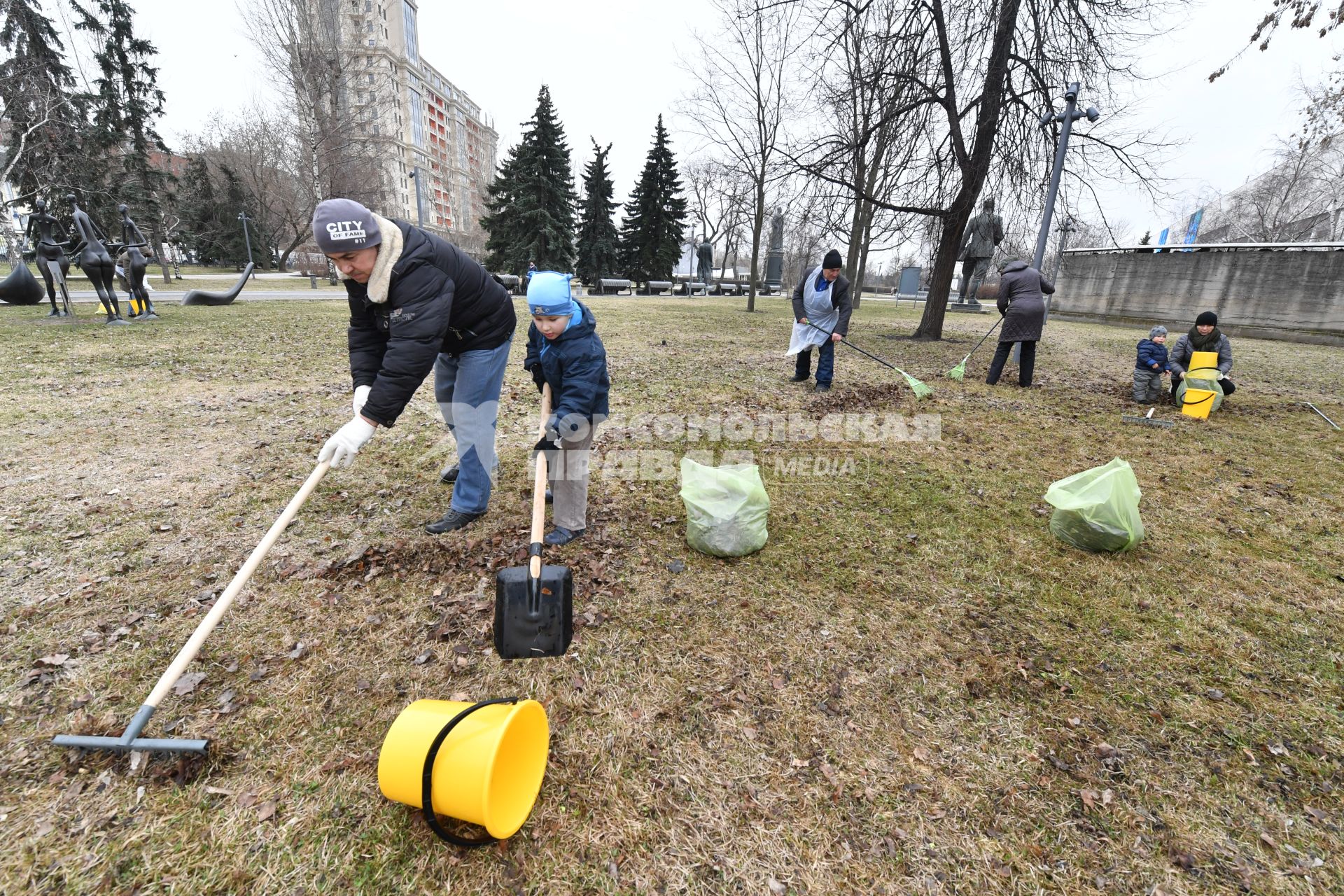 Москва. Мужчина с мальчиком на общегородском субботнике `За чистоту икусства` в парке  `Музеон` убирает сухие листья с газона.