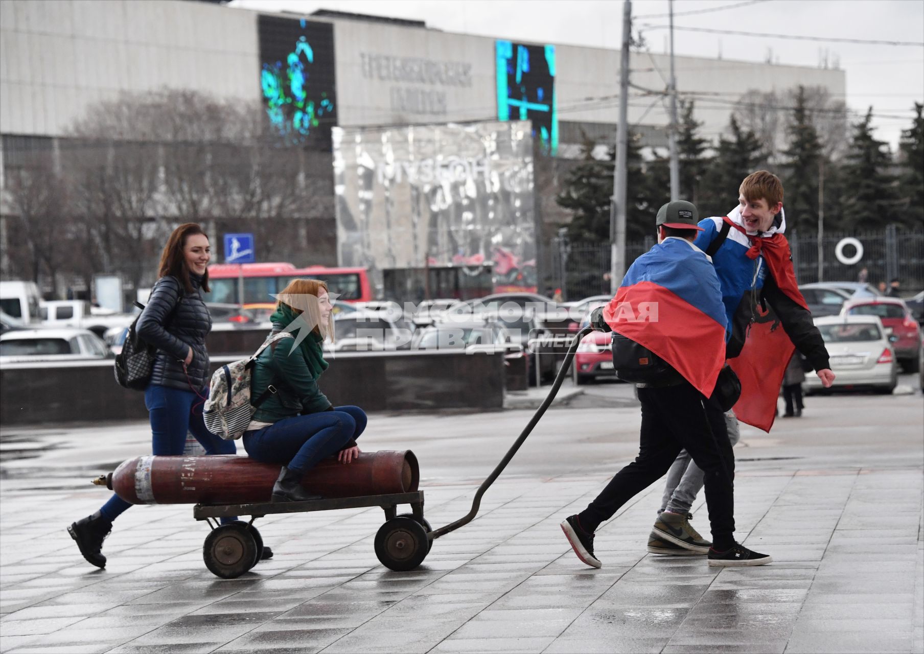 Москва. Молодые люди везут тележку с газовым баллоном, на котором сидит девушка.