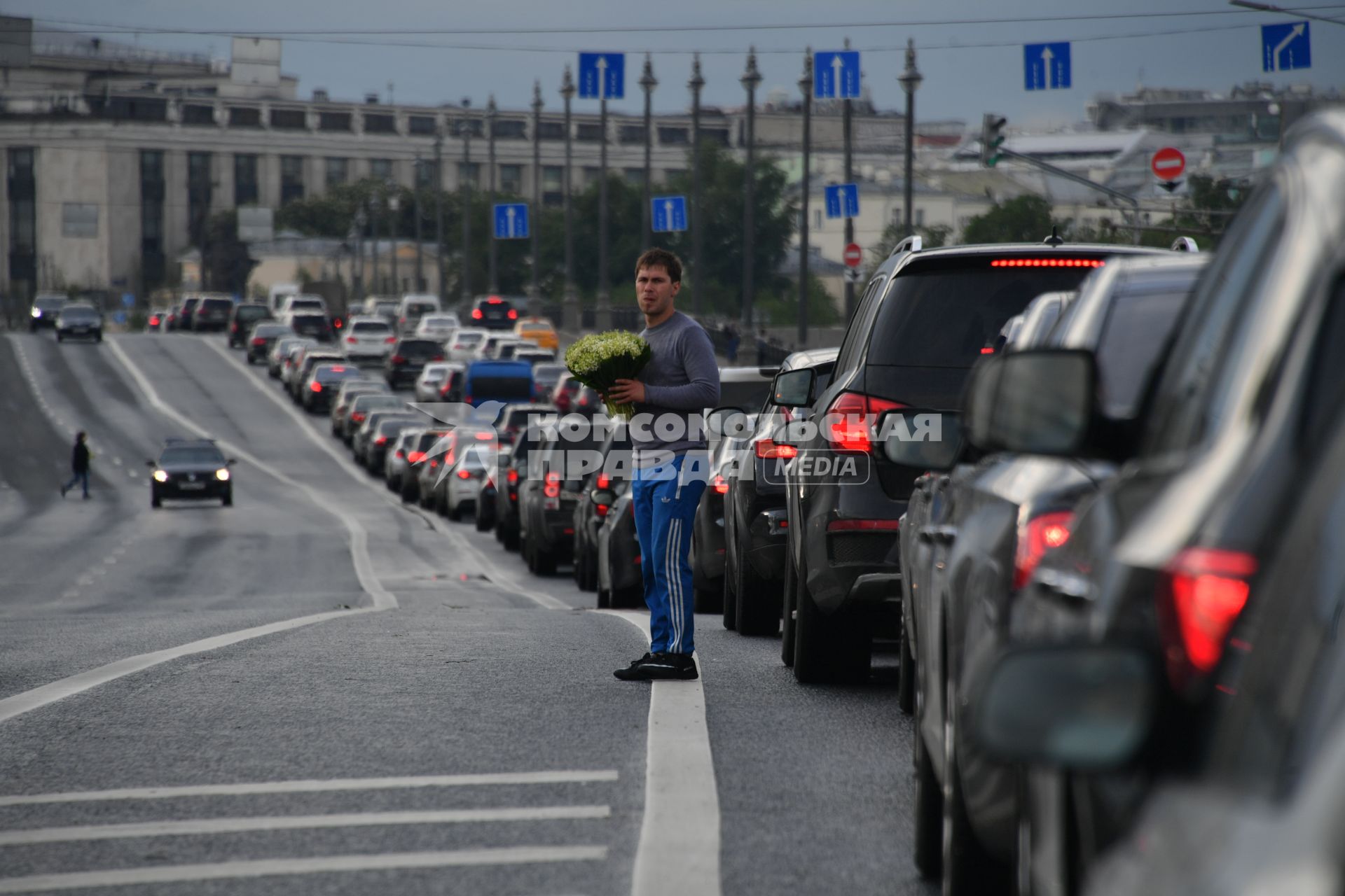 Москва. Мужчина торгует цветами на дороге среди машин.