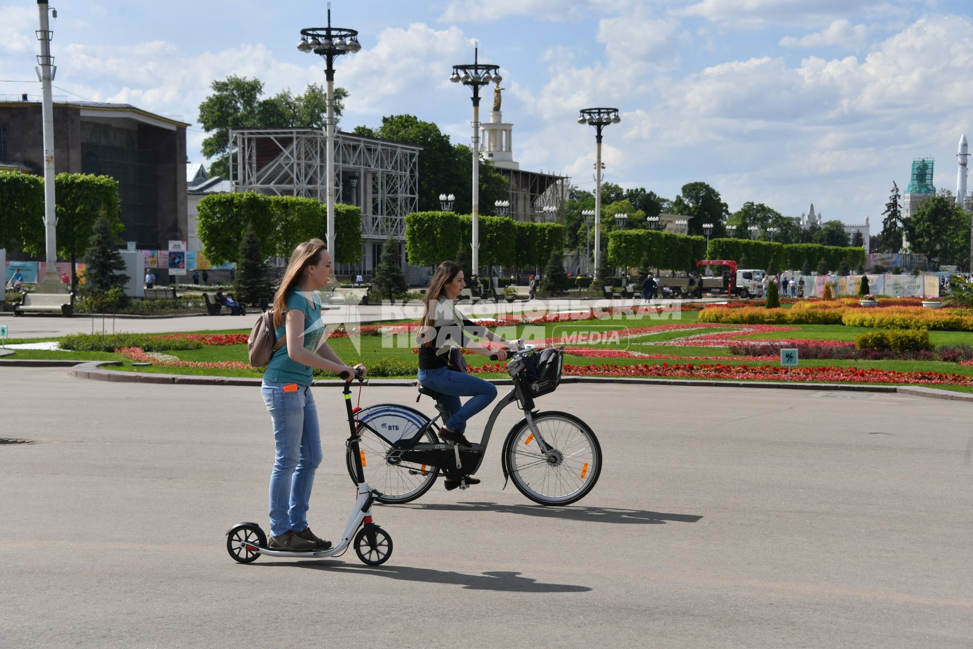 Москва.  Девушки на велосипеде и самокате на дорожках ВДНХ.