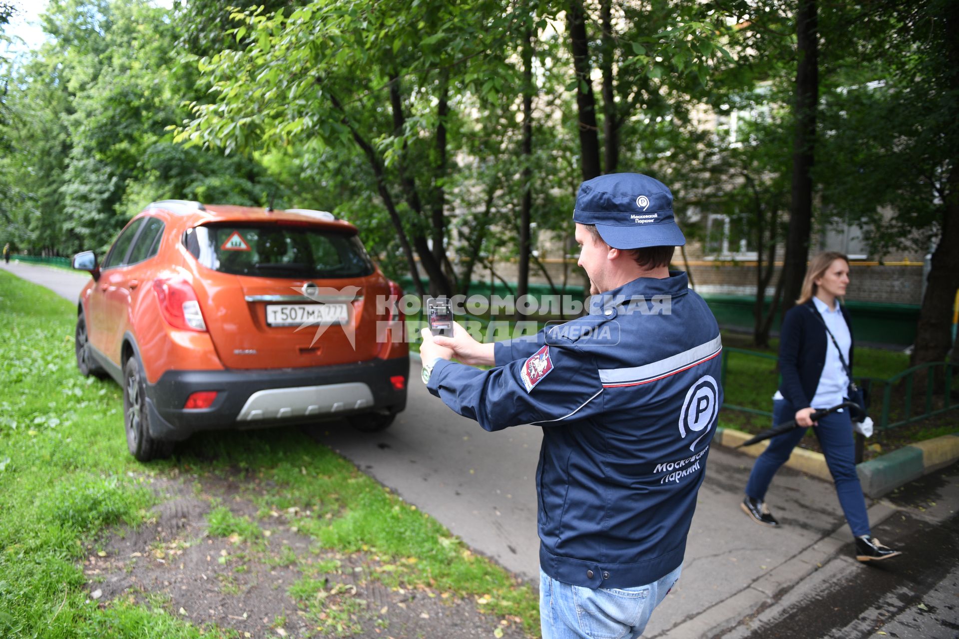 Москва. Корреспондент `Комсомольской правды` Олег Адамович в форме парковочного инспектора фотографирует припаркованный на газоне автомобиль.