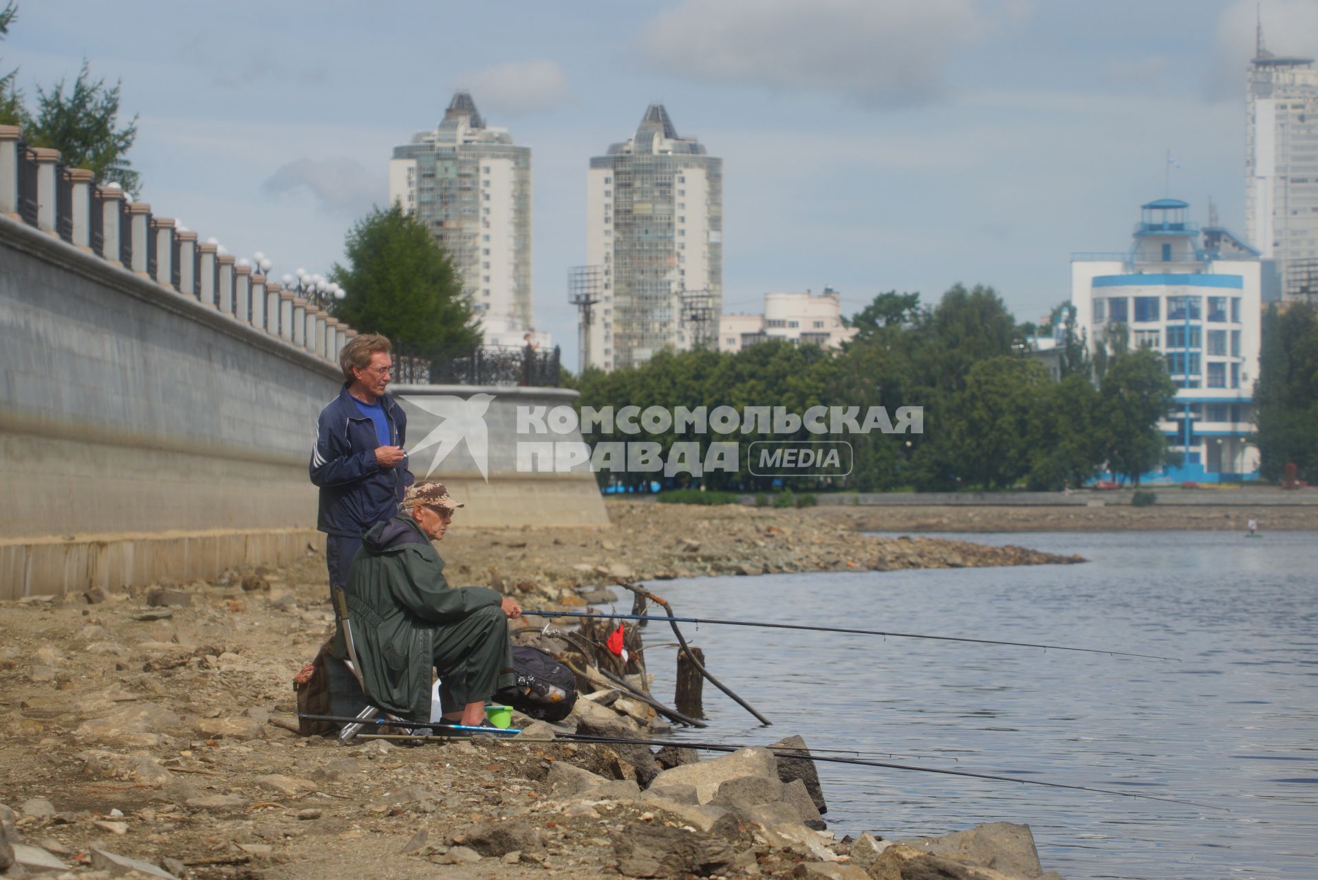 Екатеринбург. Мужчины ловят рыбу на обмелевшем  берегу набережной городского пруда.