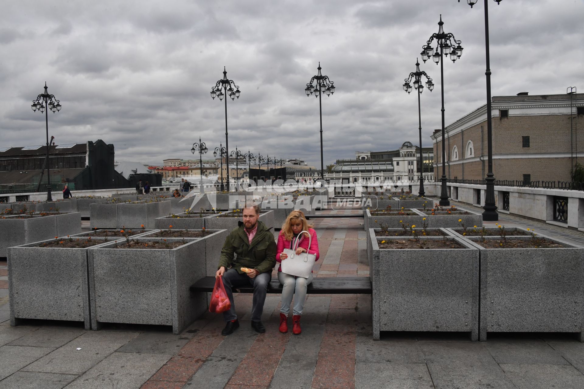 Москва.  Женщина и мужчина сидят на скамейках у Патриаршего моста.