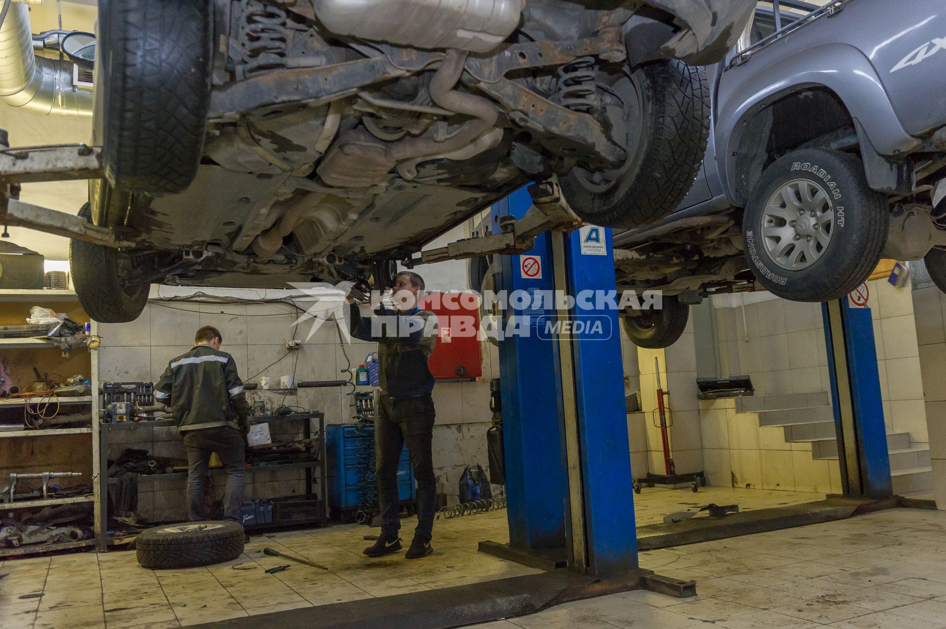 Санкт-Петербург. Автомеханники  производят ремонт колеса автомобиля в автосервисе.