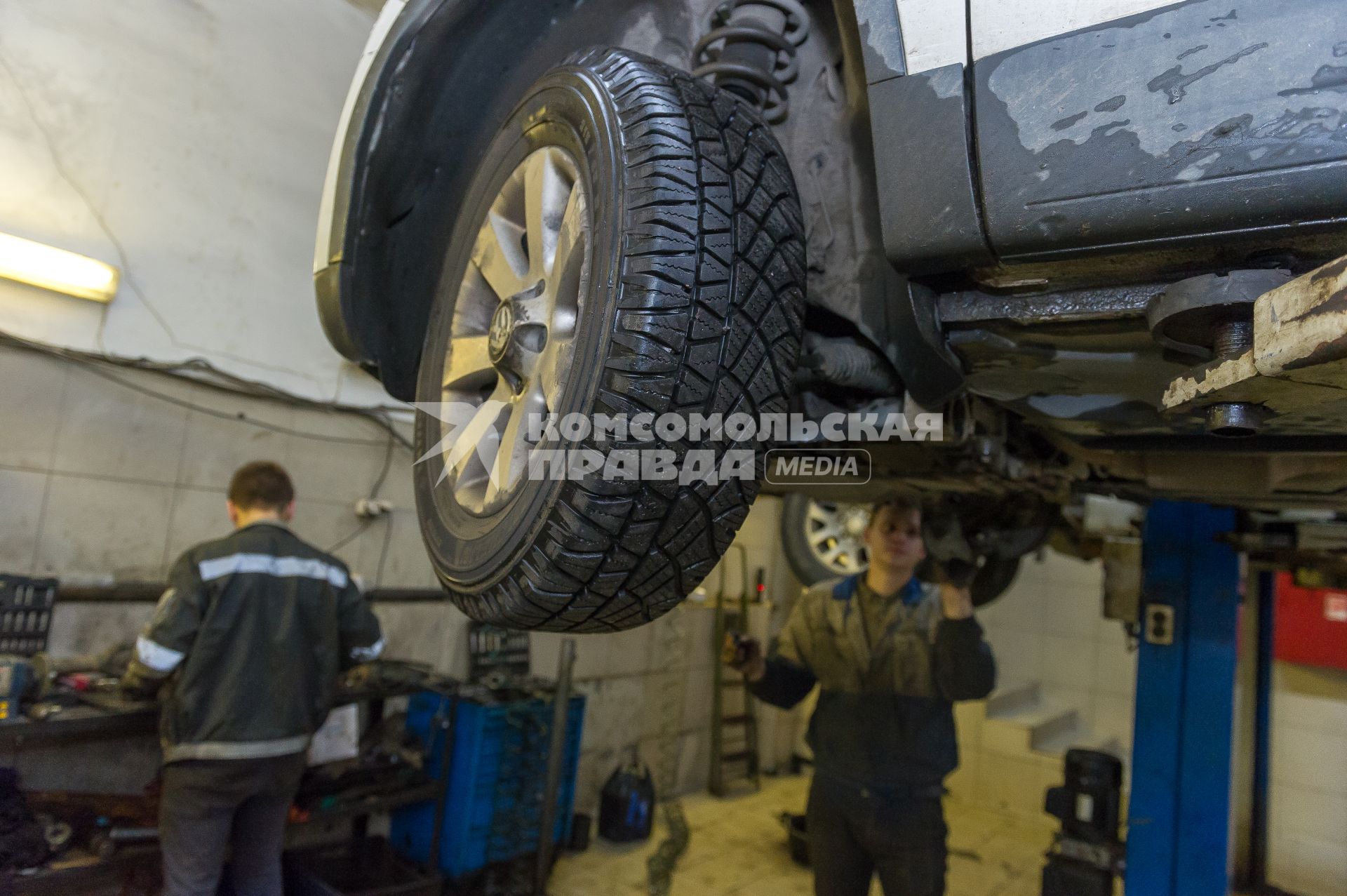 Санкт-Петербург. Автомеханники  производят ремонт колеса автомобиля в автосервисе.