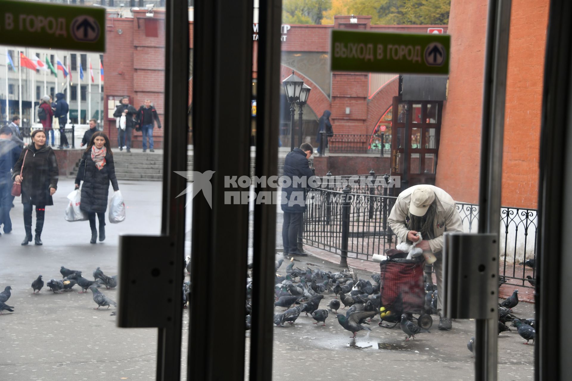 Москва. Пожилой мужчина кормит голубей у дверей метро на площади Революции.