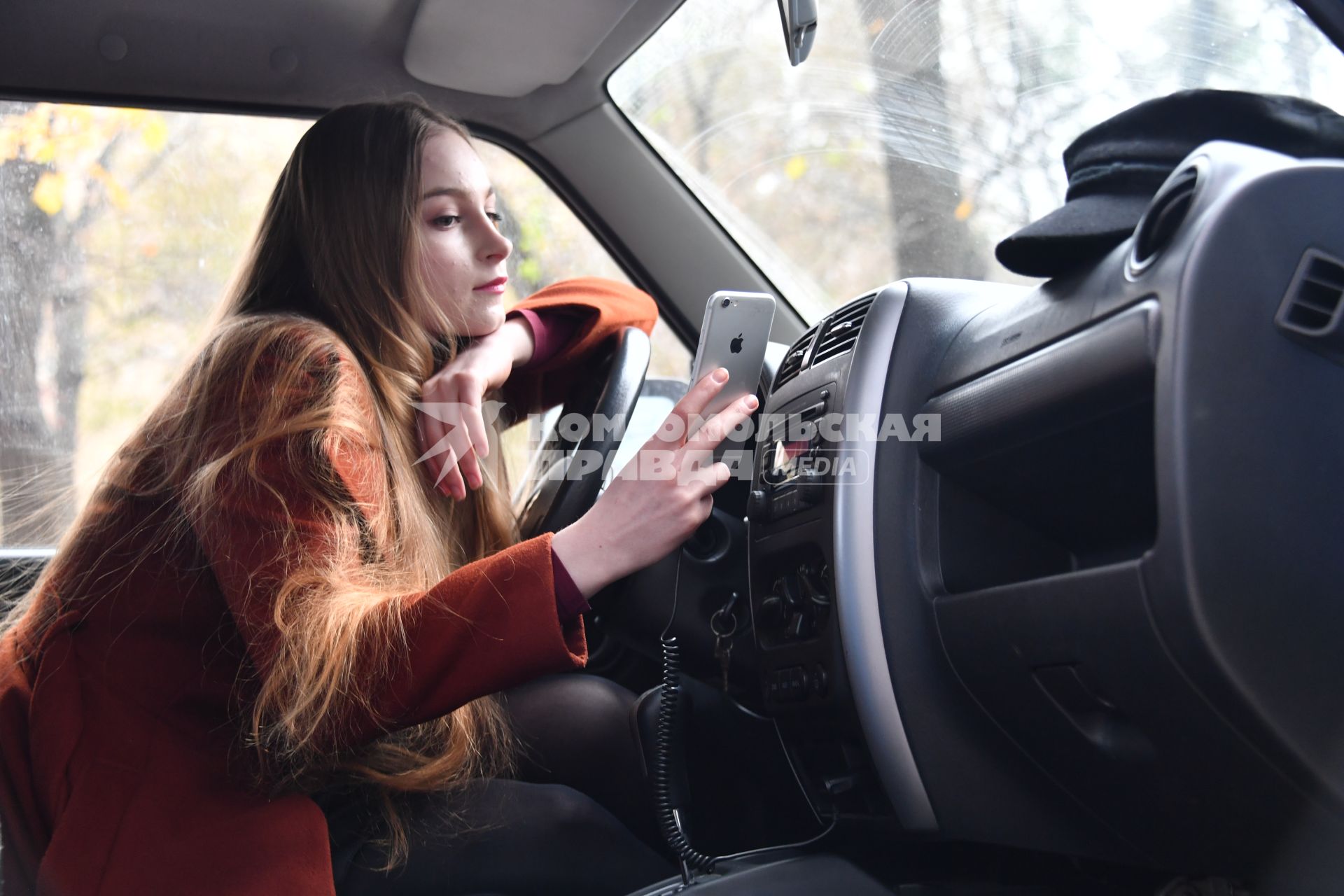 Москва.   Девушка заряжает мобильный телефон в салоне автомобиля.