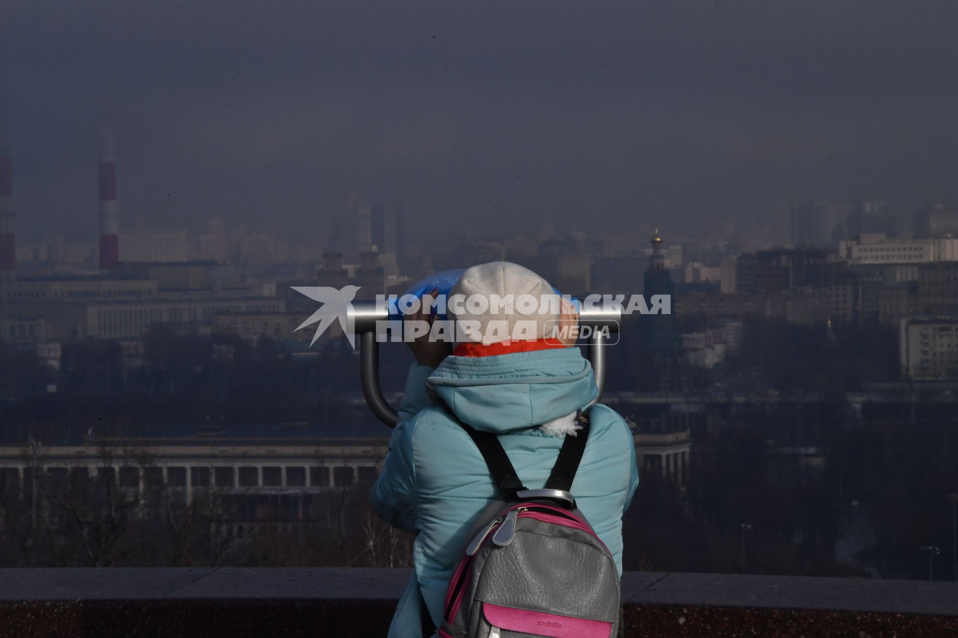 Москва.  Женщина смотрит в бинокль на смотровой площадке Воробьевых гор.