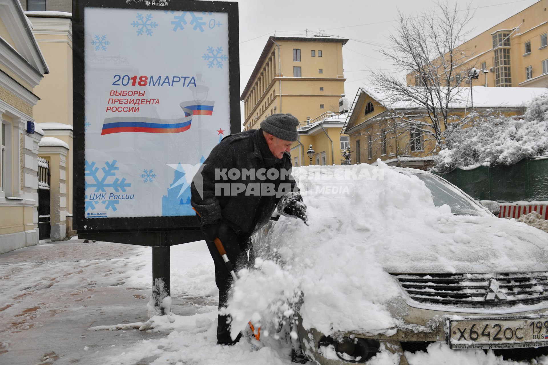 Москва.  Мужчина очищает машину от снега.