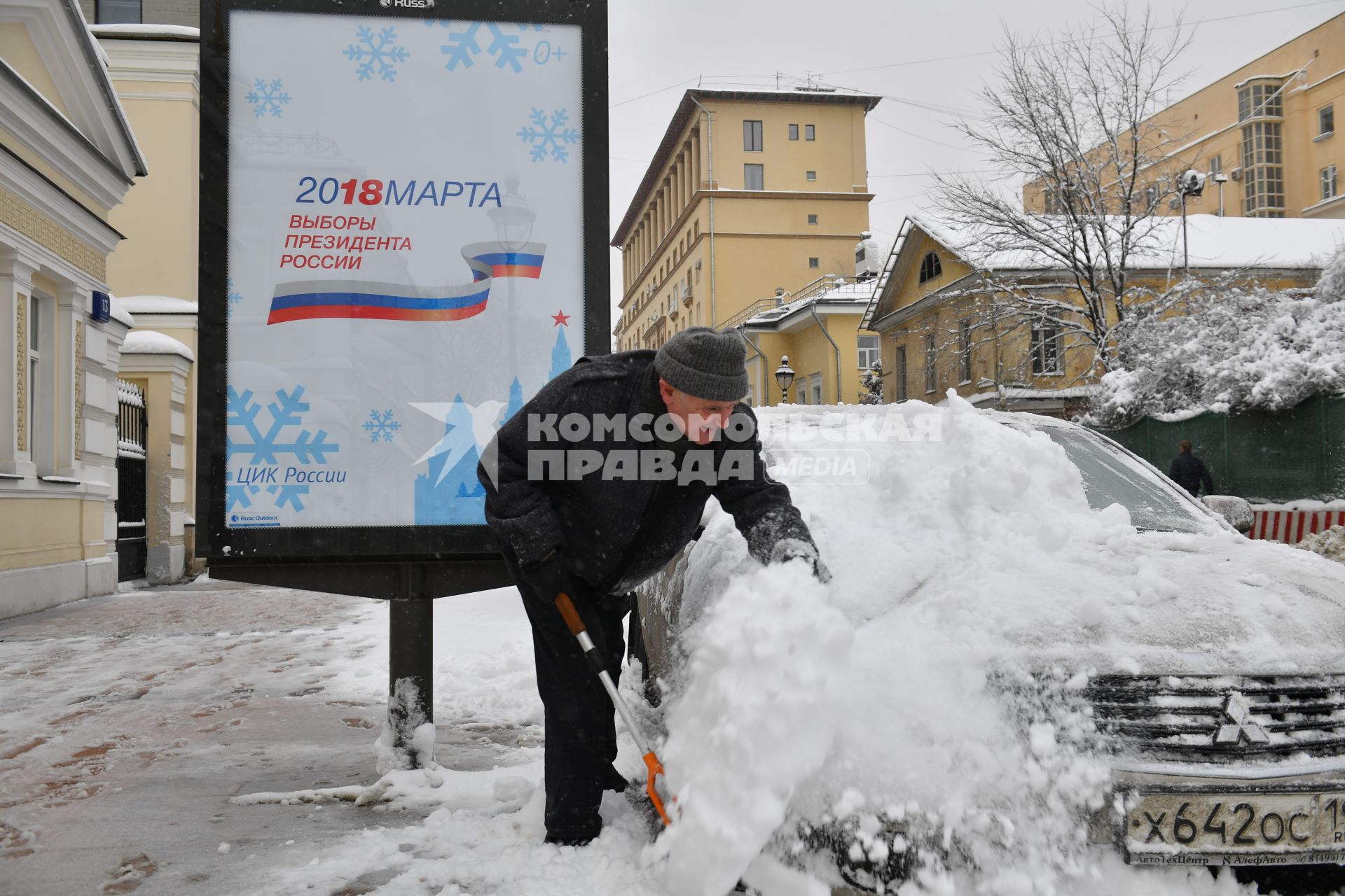 Москва.  Мужчина очищает машину от снега.