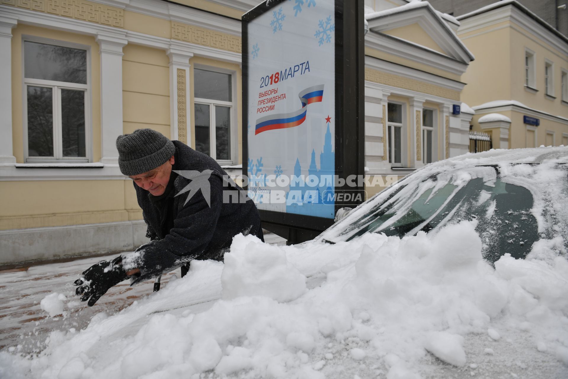 Москва.  Мужчина очищает машину от снега.