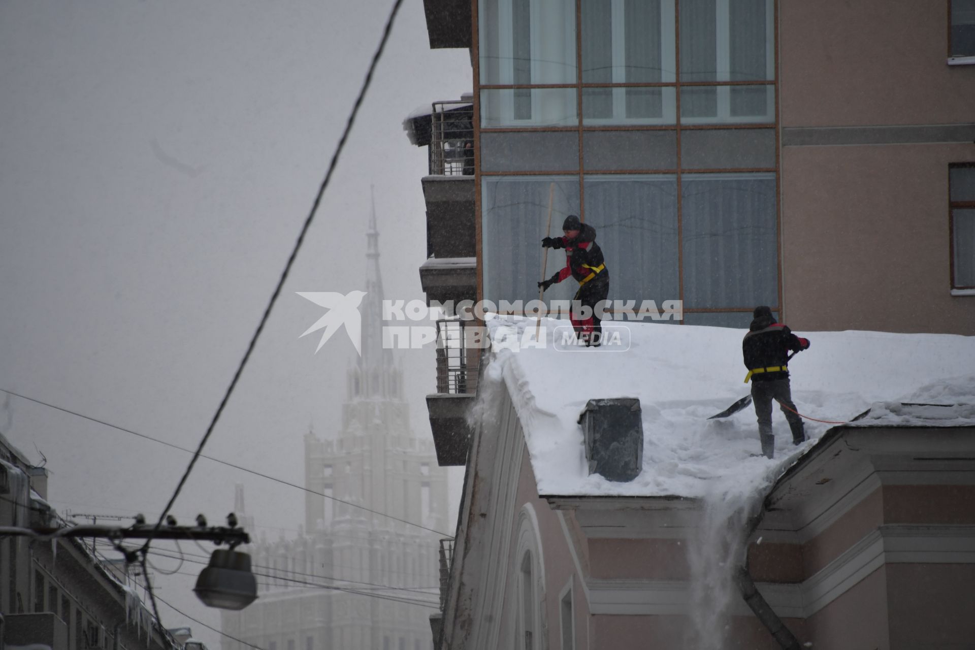 Москва.   Сотрудники коммунальной службы счищают снег с крыши дома.