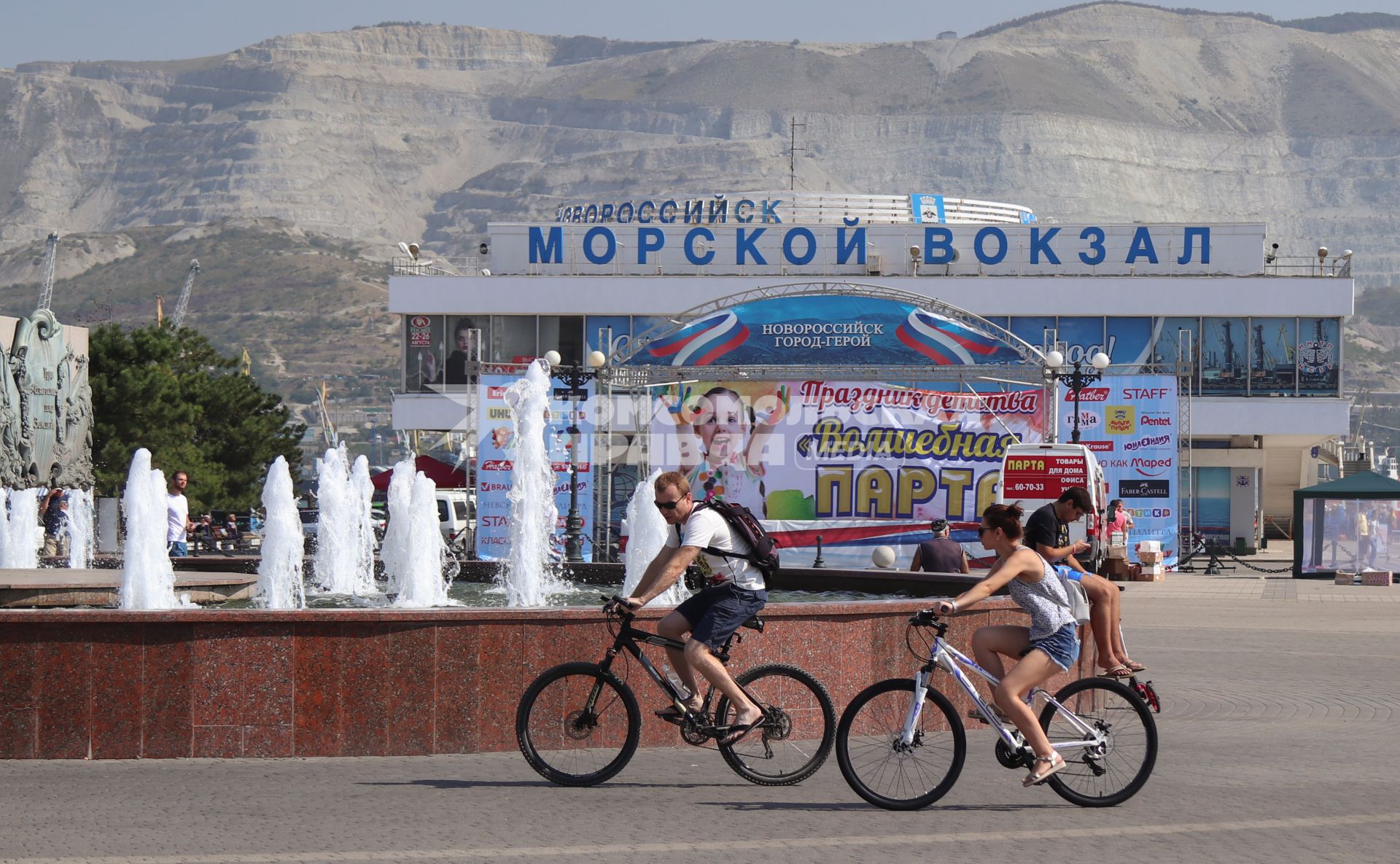 Новороссийск.  Мужчина с девушкой на велосипедах у Морского вокзала.