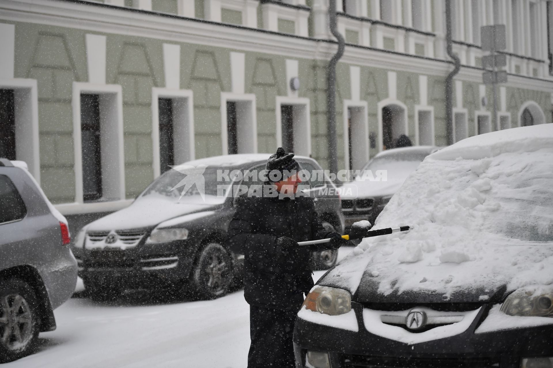 Москва. Мужчина очищает машину от снега   в Хлебном переулке.