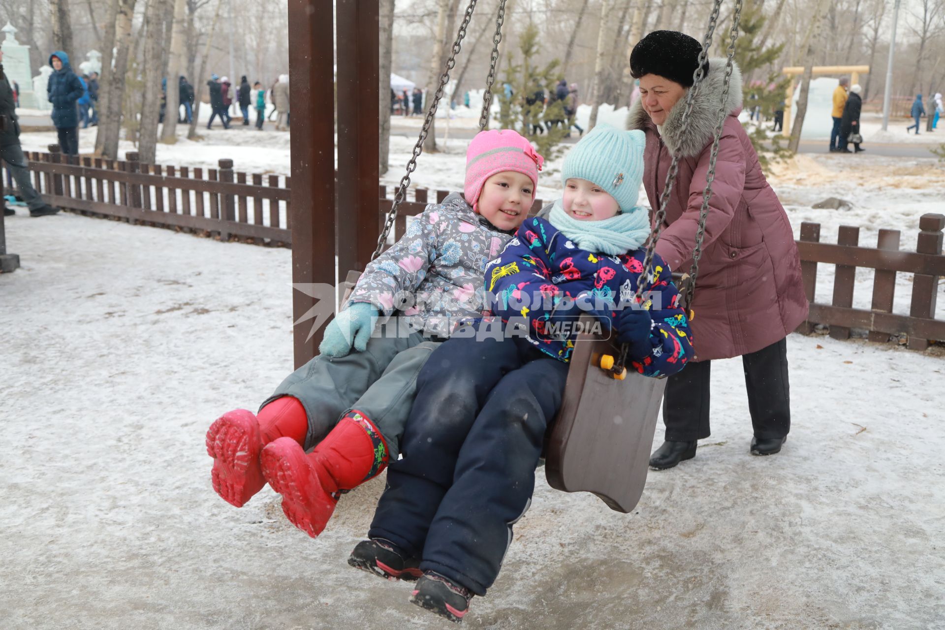 Красноярск. Бабушка качает внучек на качелях.